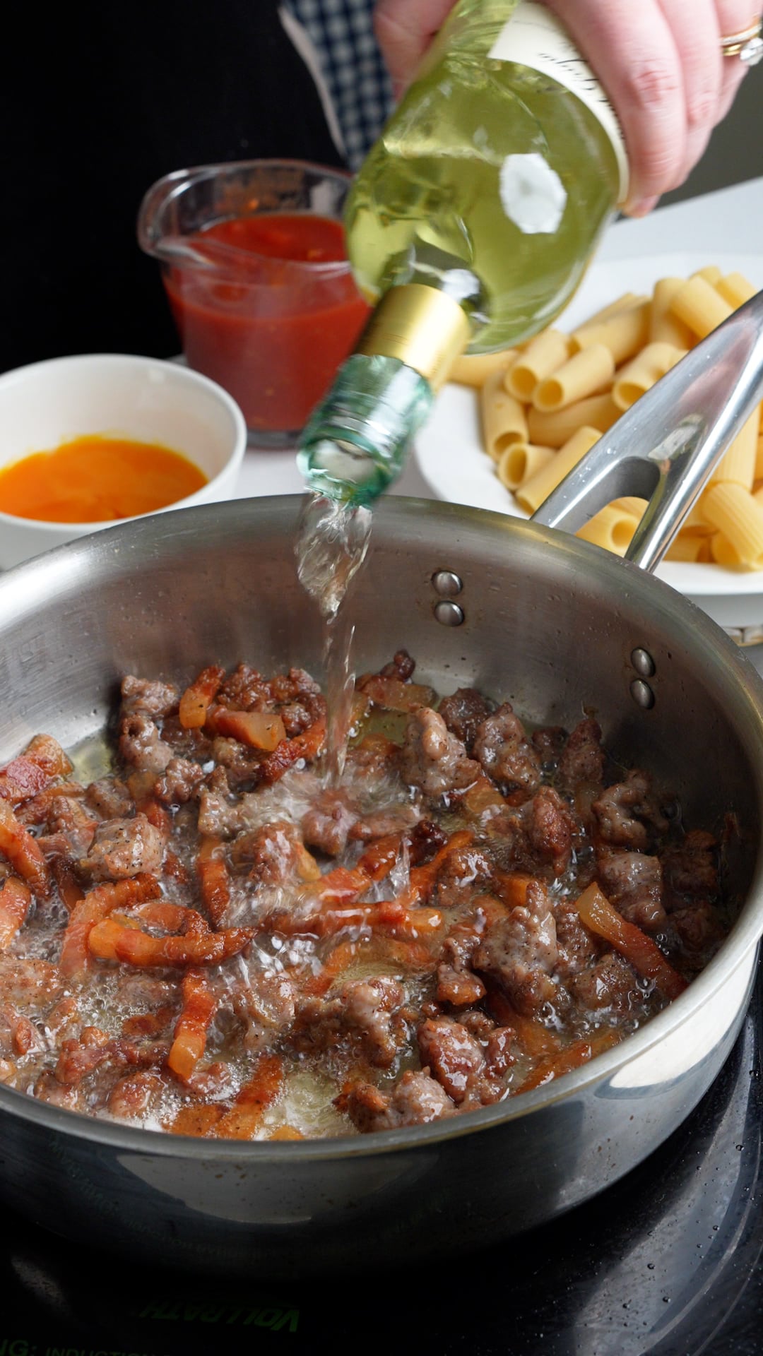 White wine being poured into a pan with sausage and guanciale in it