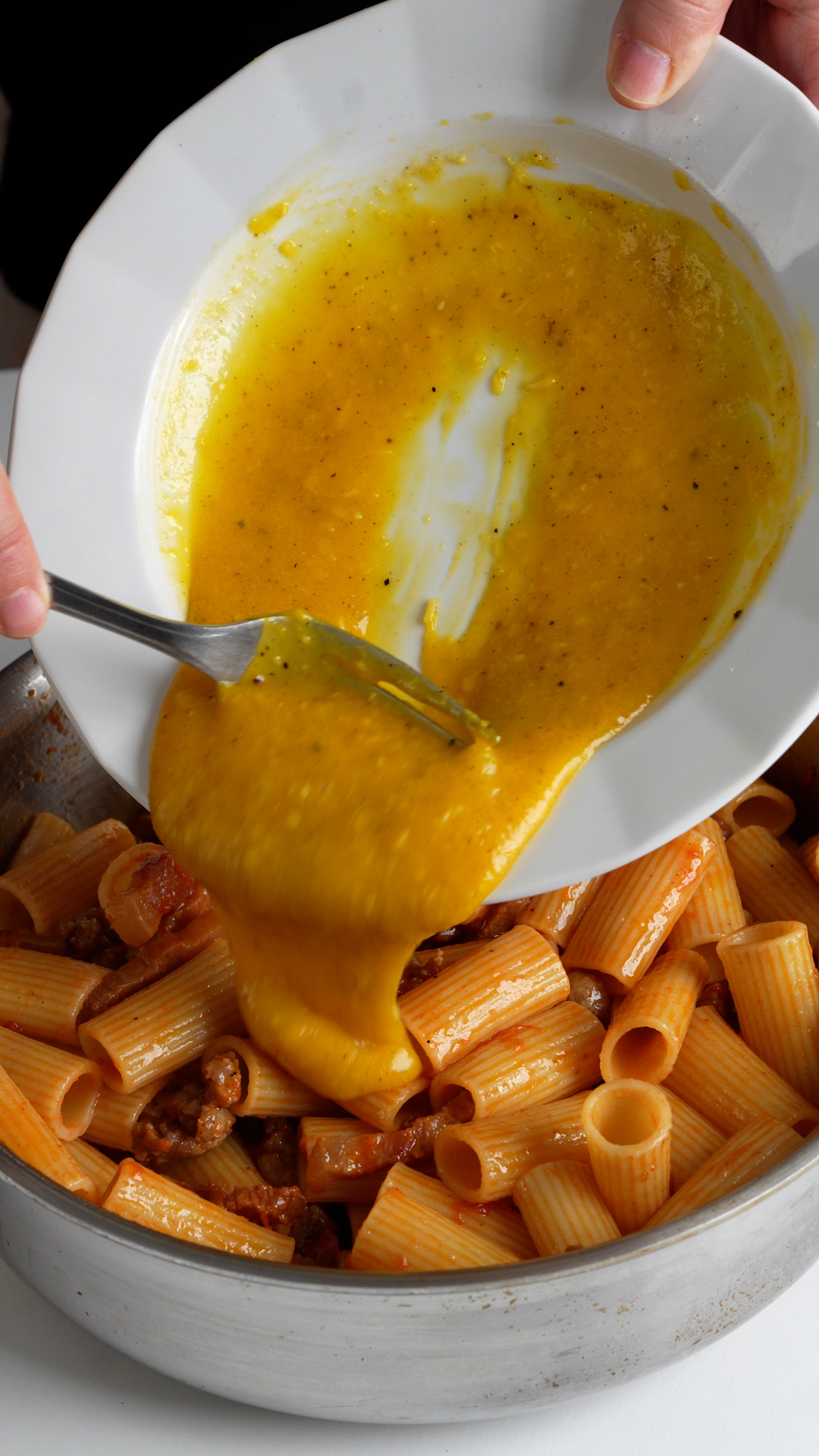 Beaten eggs and pecorino being poured onto pasta in a pan