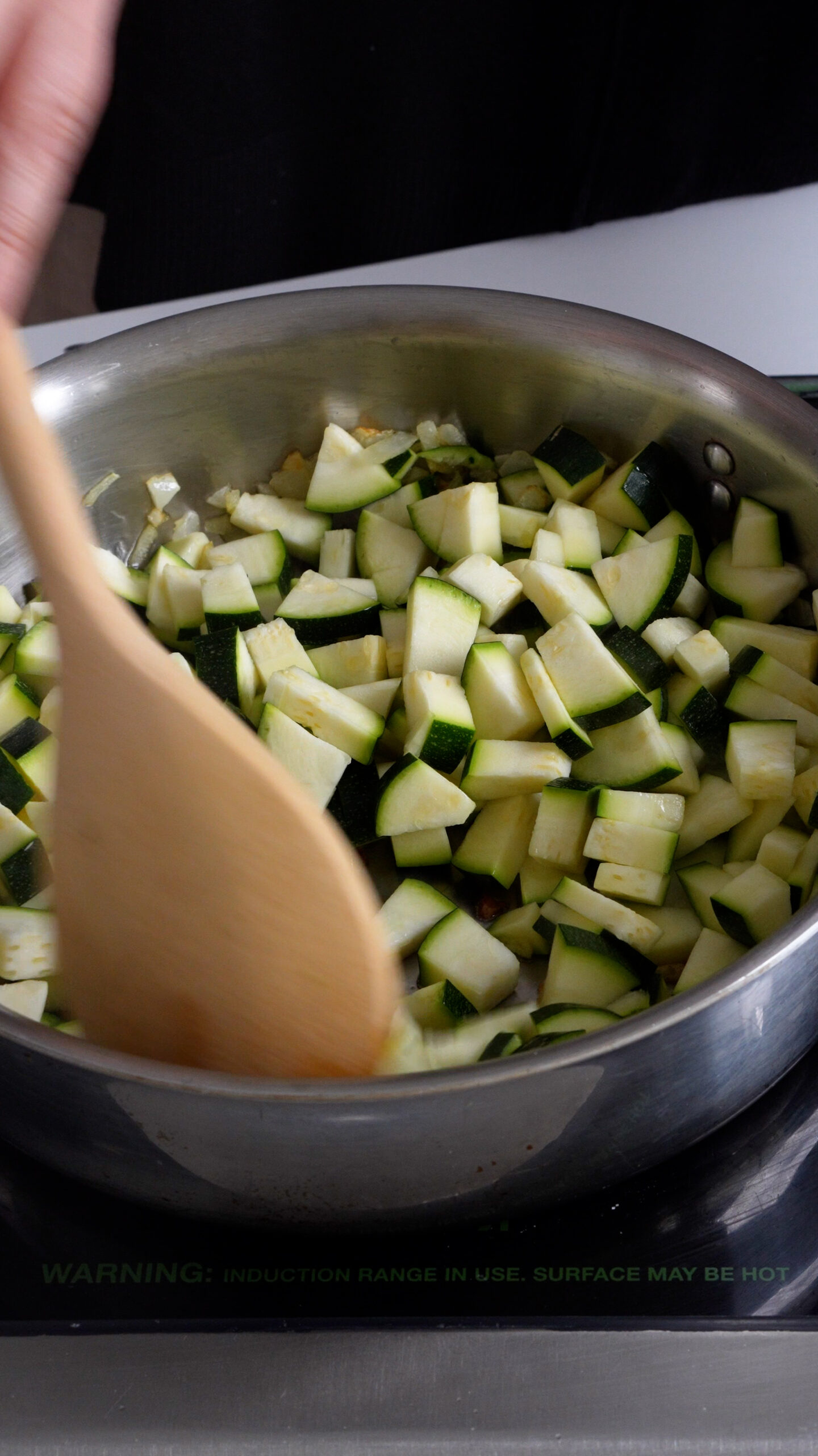 Diced zucchini in a pan being stirred with a wooden spoon