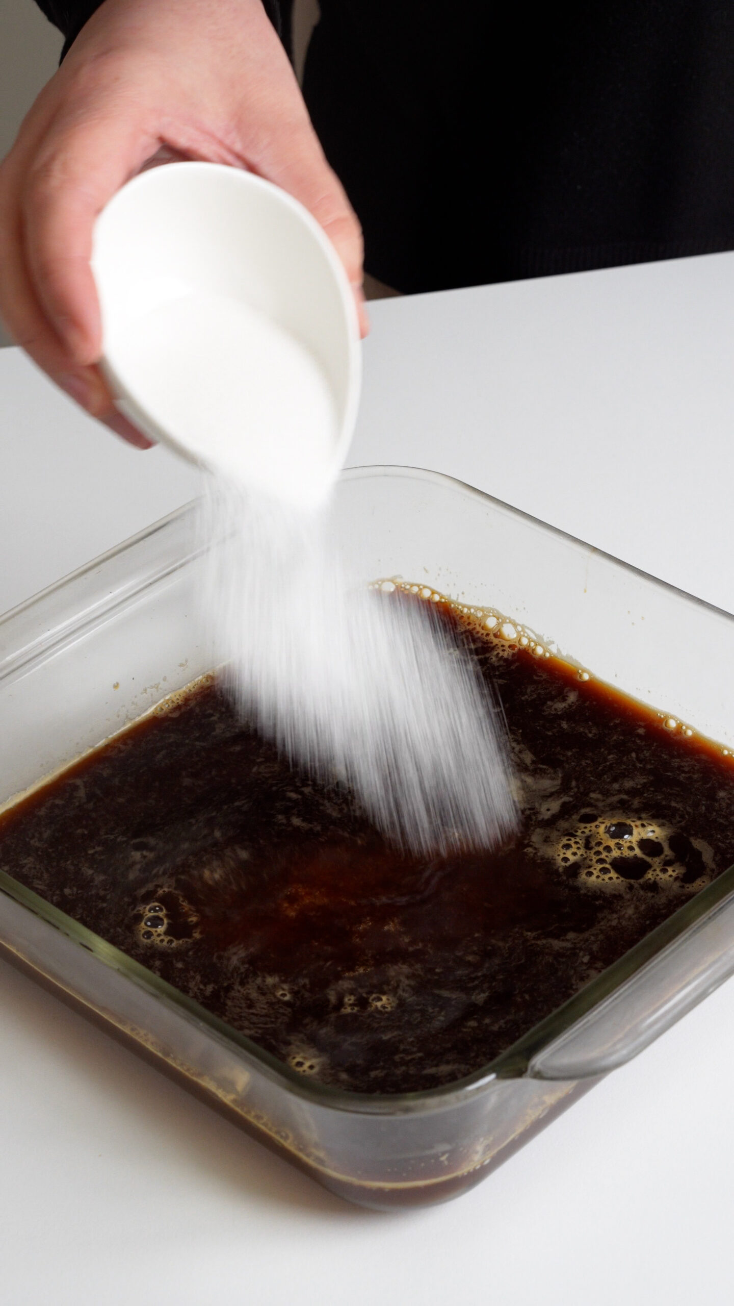 Sugar being poured into a square dish with espresso in it