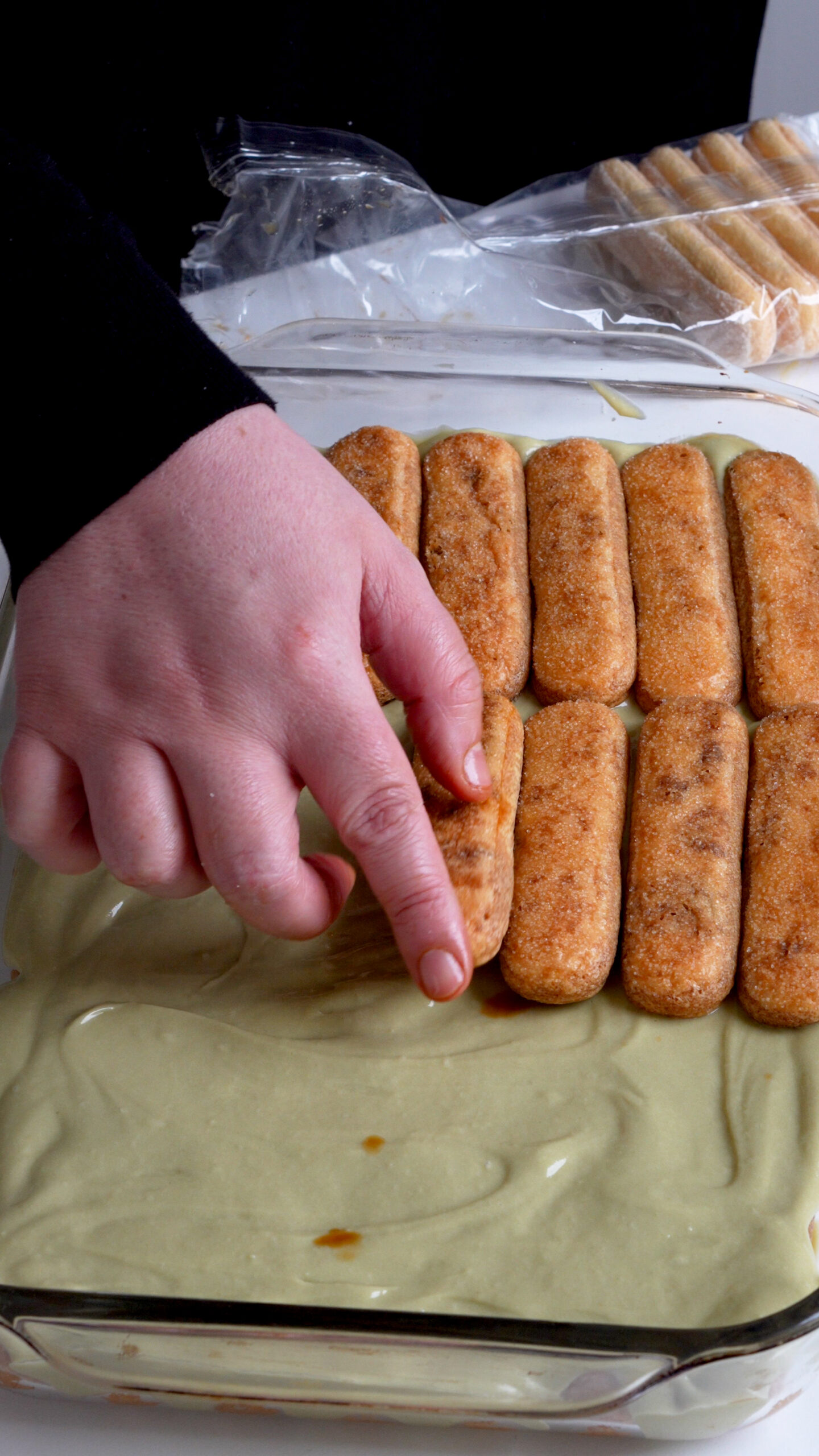 Second layer of espresso-soaked ladyfinger cookies being placed in baking dish