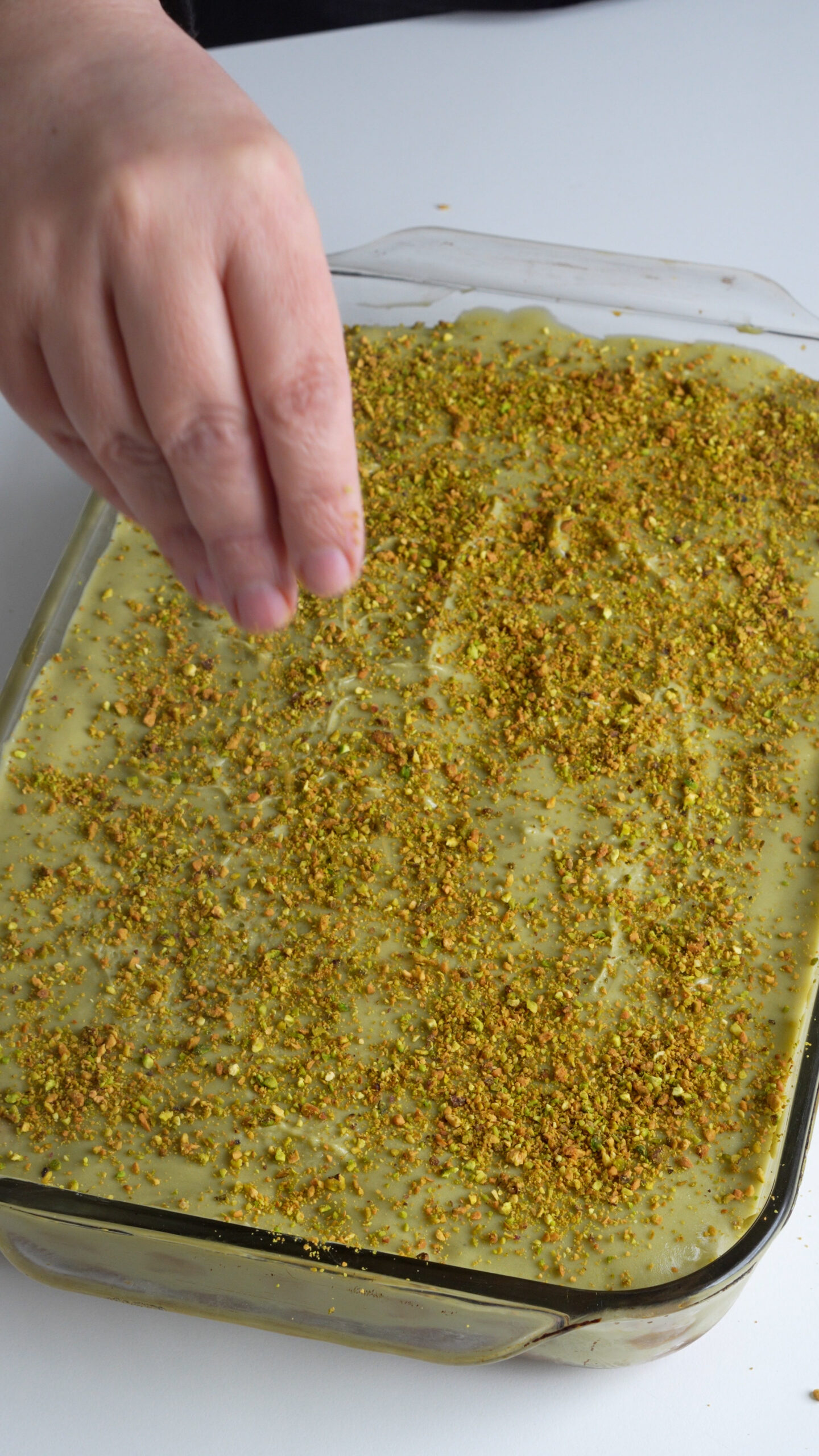Chopped pistachios being placed onto pistachio tiramisu