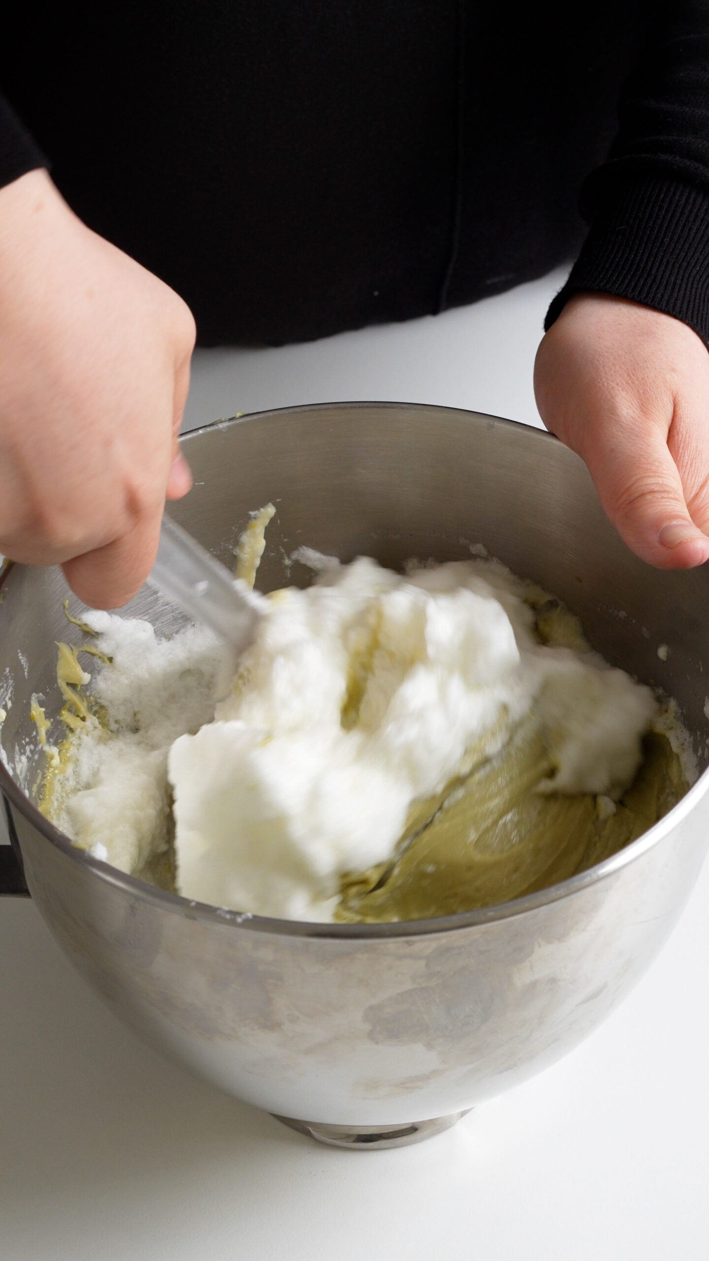 Egg whites being folded into pistachio tiramisu cream in the bowl of a stand mixer