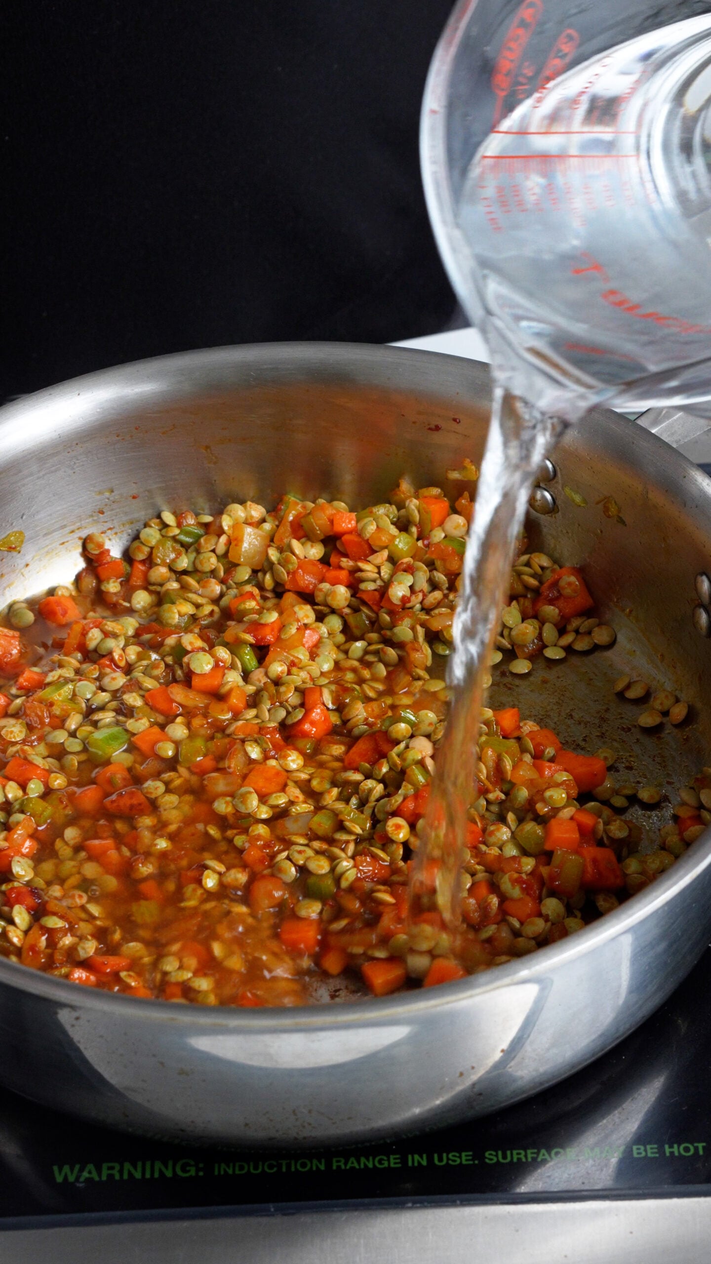 Water being added to a pan with carrot, celery, onion and dried lentils