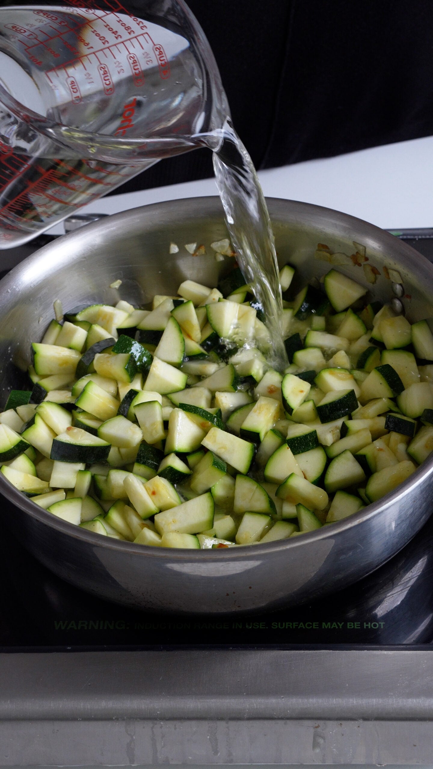 Water being added to diced zucchini in a pan