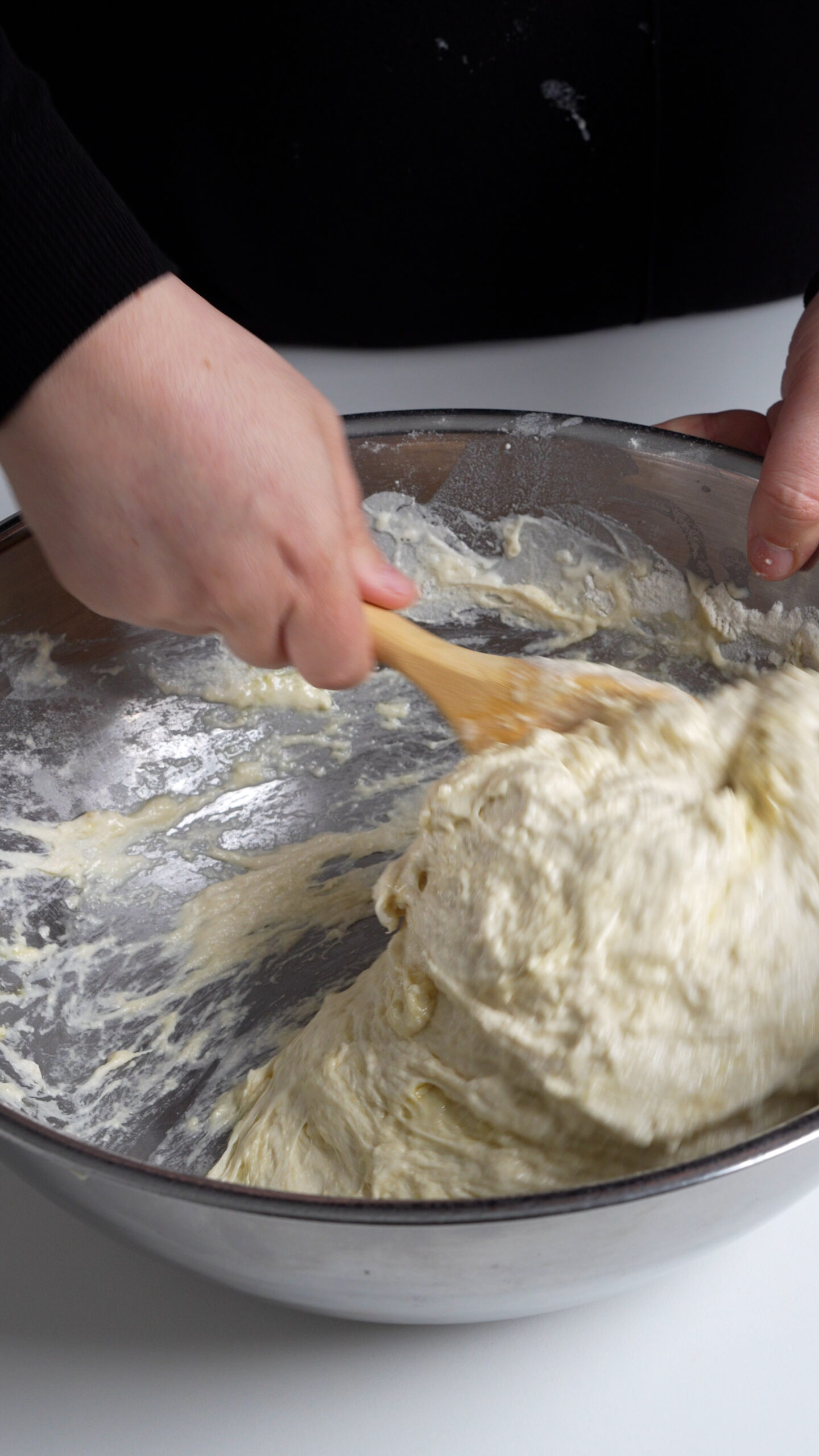 Focaccia dough in a bowl being mixed with a wooden spoon