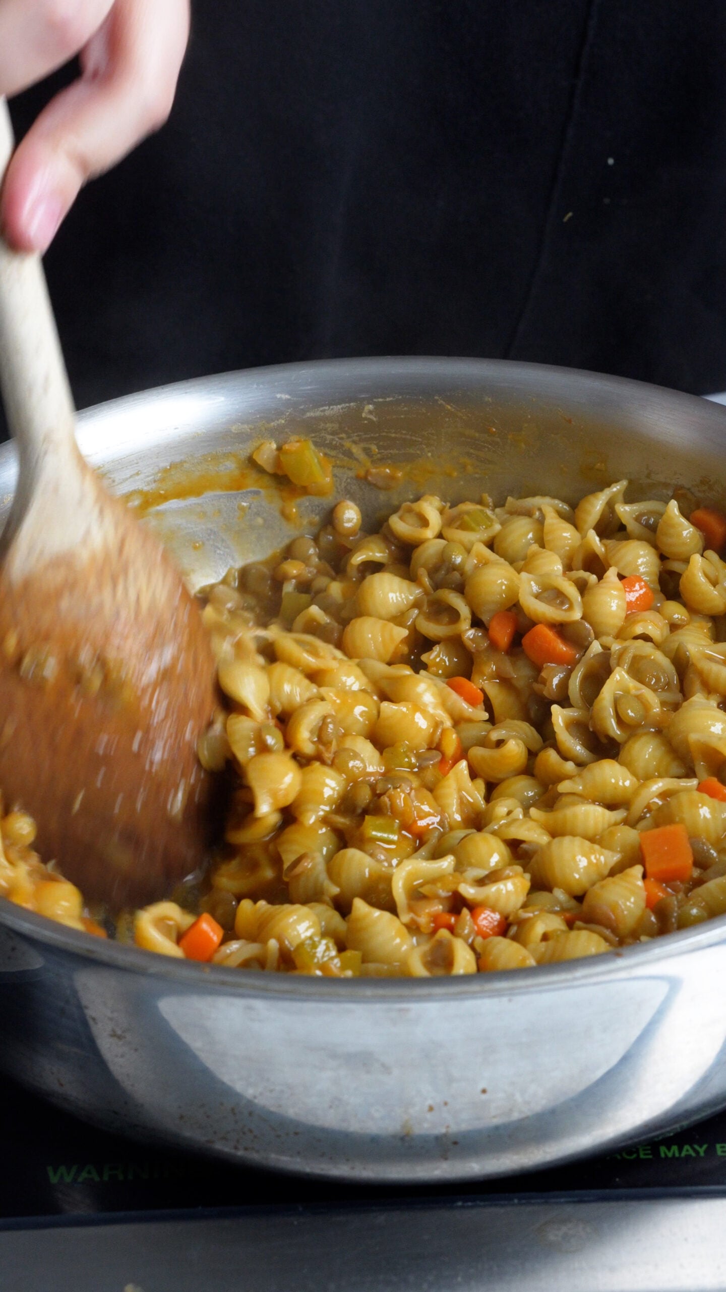 Pasta and lentils in pan being stirred with a wooden spoon