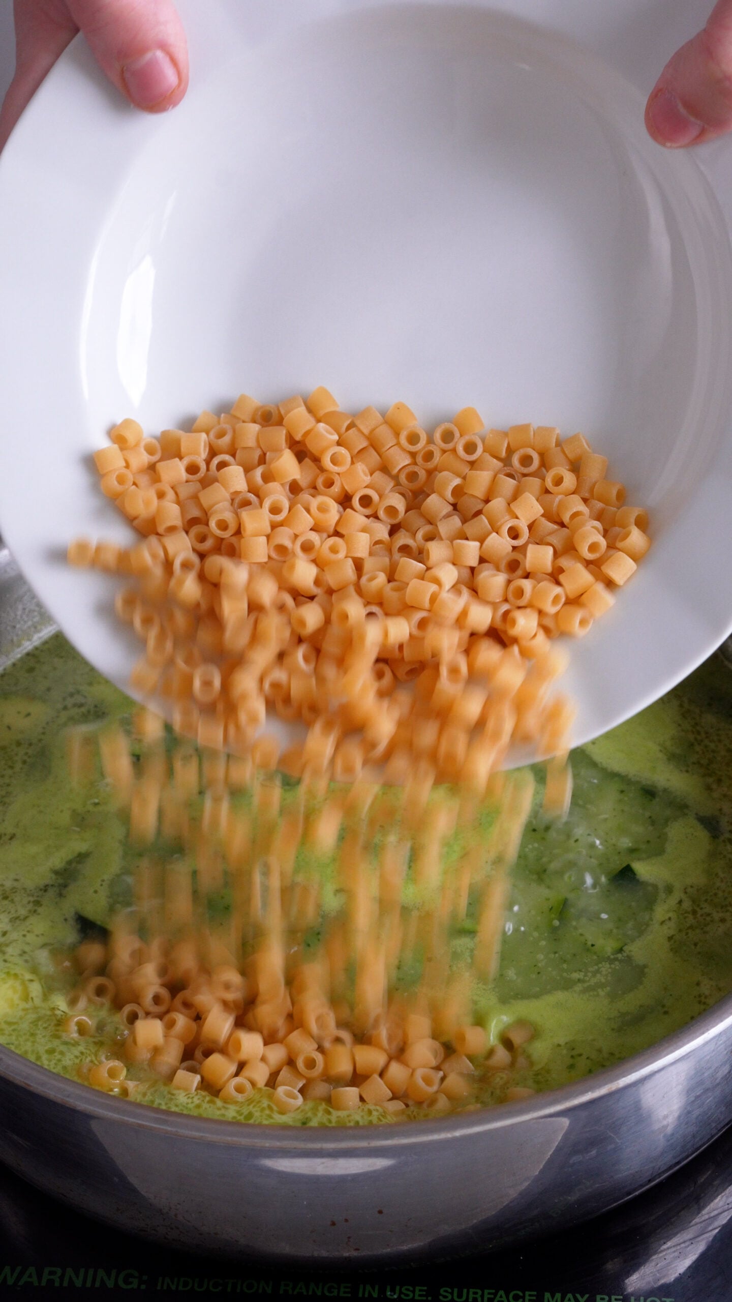 Ditali pasta being added to a pan with zucchini and water