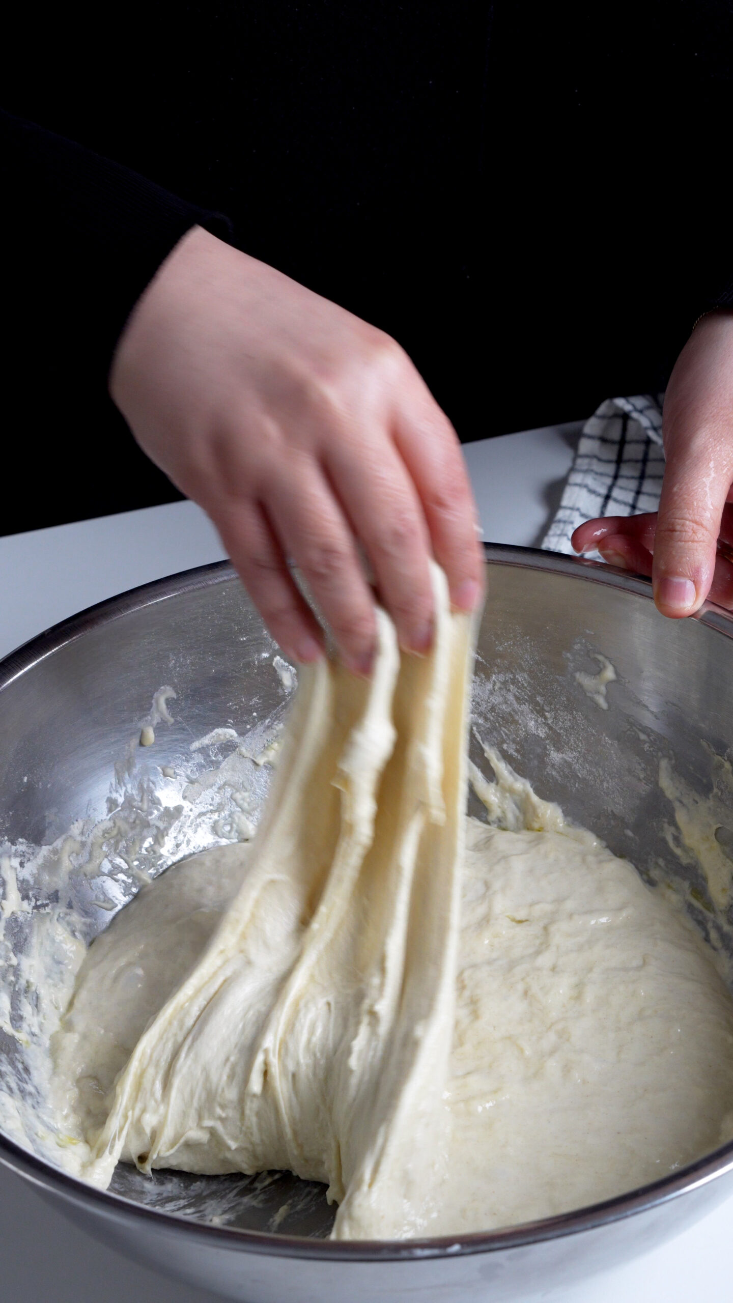 Focaccia dough in a bowl being stretched out with a hand