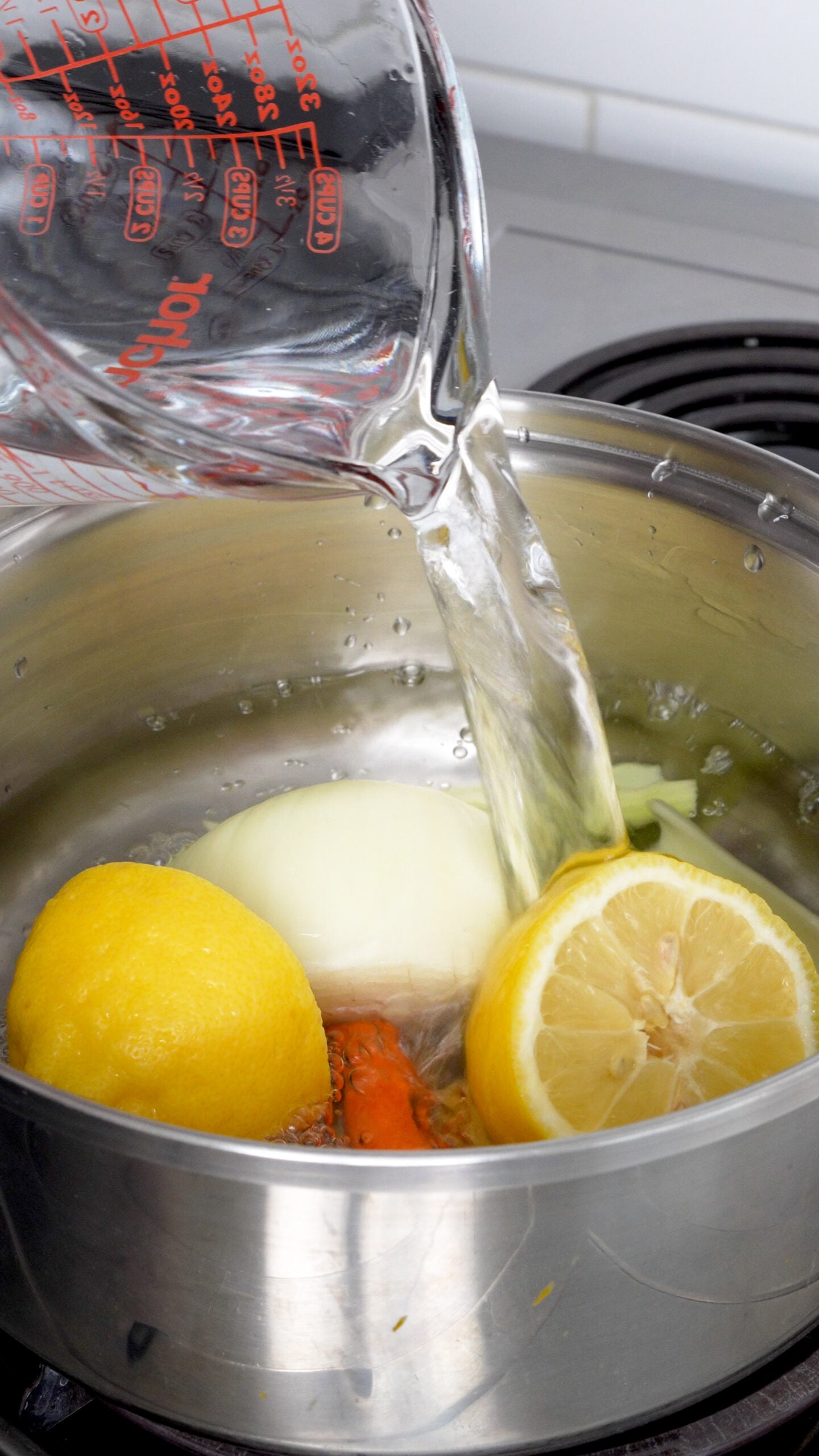 Water being poured into a saucepan with lemons, carrots, celery and onion in it