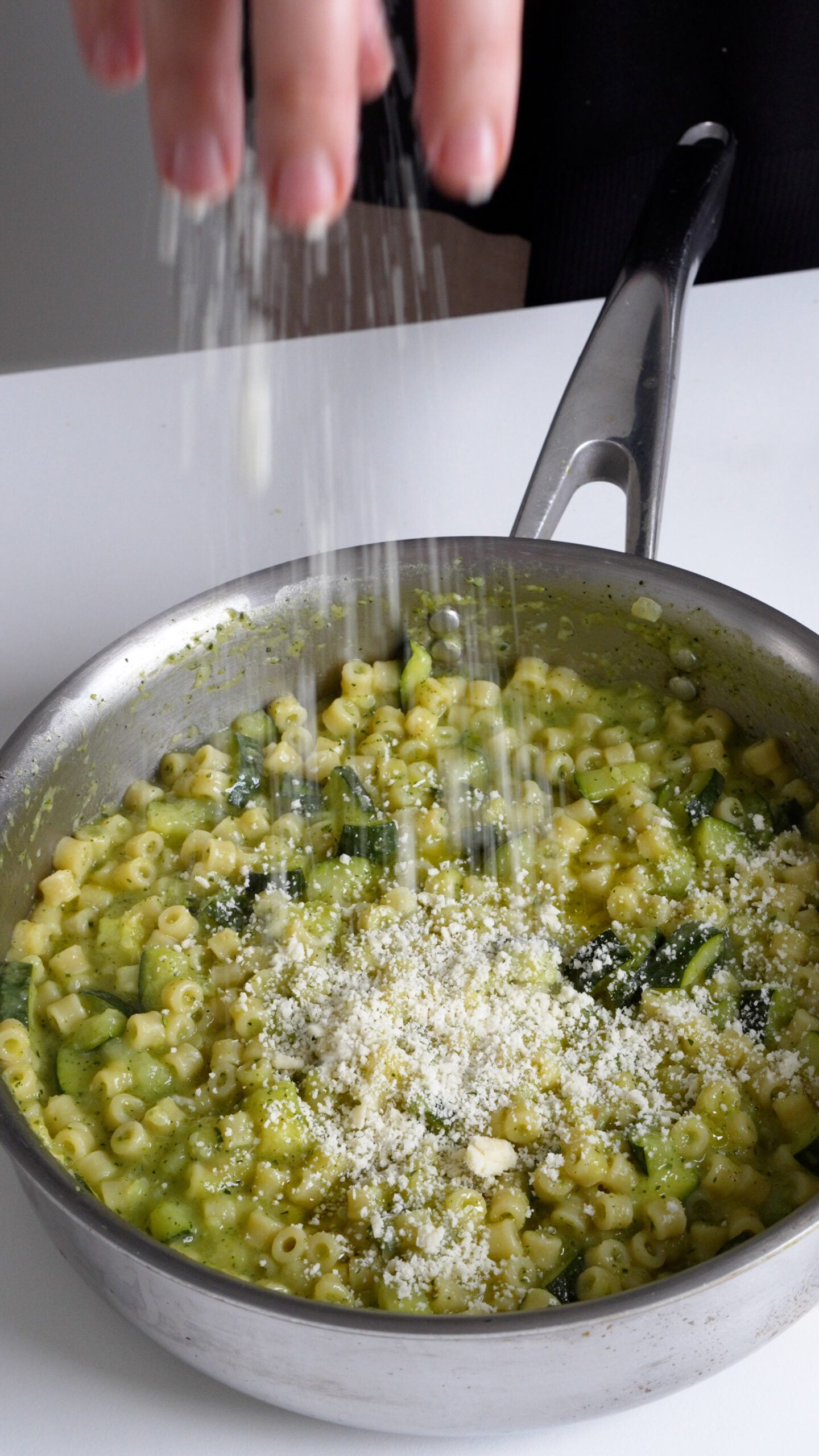 Parmigiano reggiano being added to a pan with zucchini pasta in it