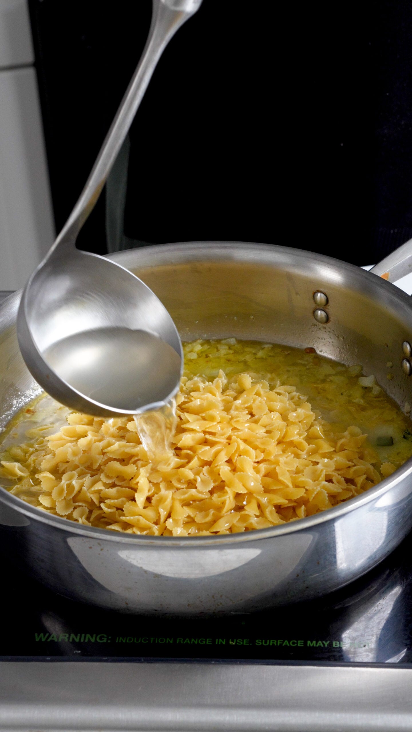 Lemon broth being ladled into a sauce pan with small pasta in it