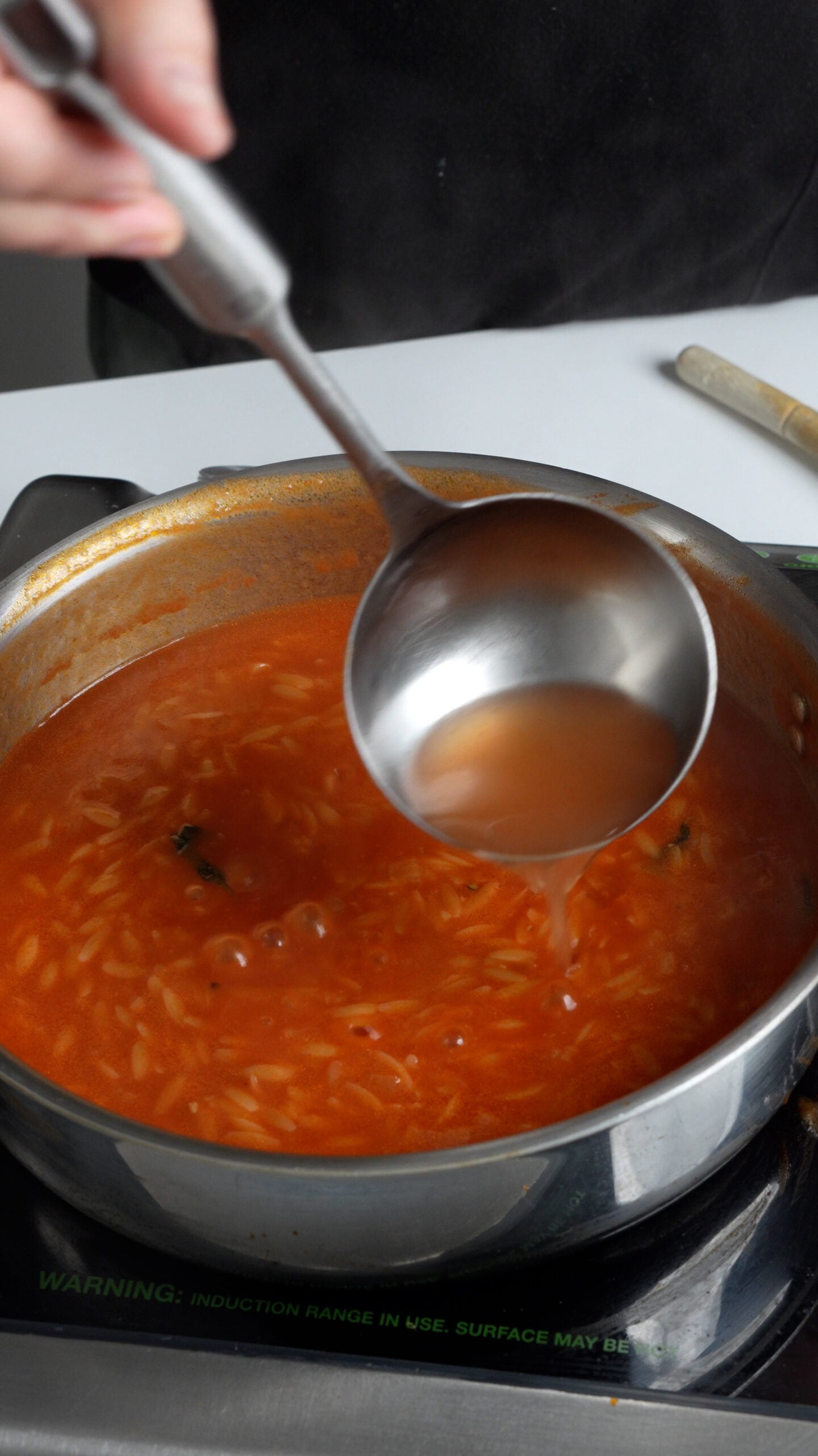 Tomato broth being ladled into a pan of tomato pastina