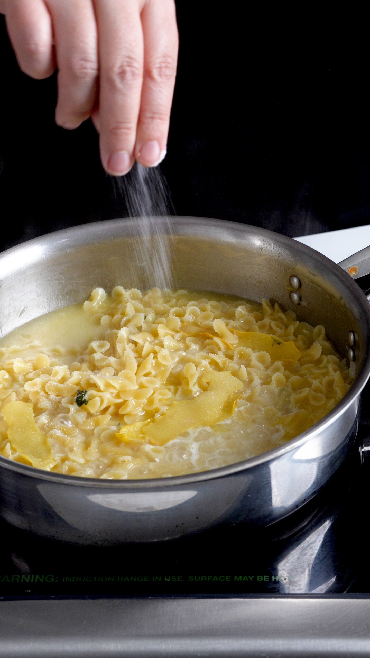 Salt being sprinkled into a sauce pan with small pasta and lemon rinds in it