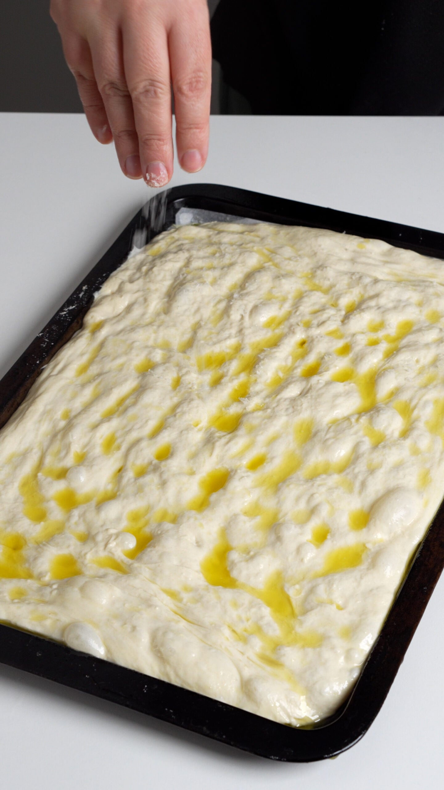 Focaccia dough on a baking sheet topped with olive oil, water and salt