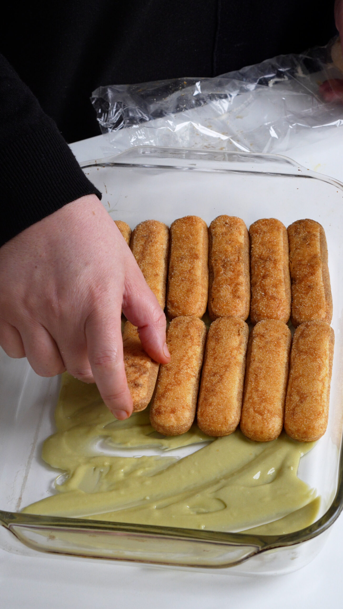 Espresso-soaked ladyfinger cookies being layered into a baking dish