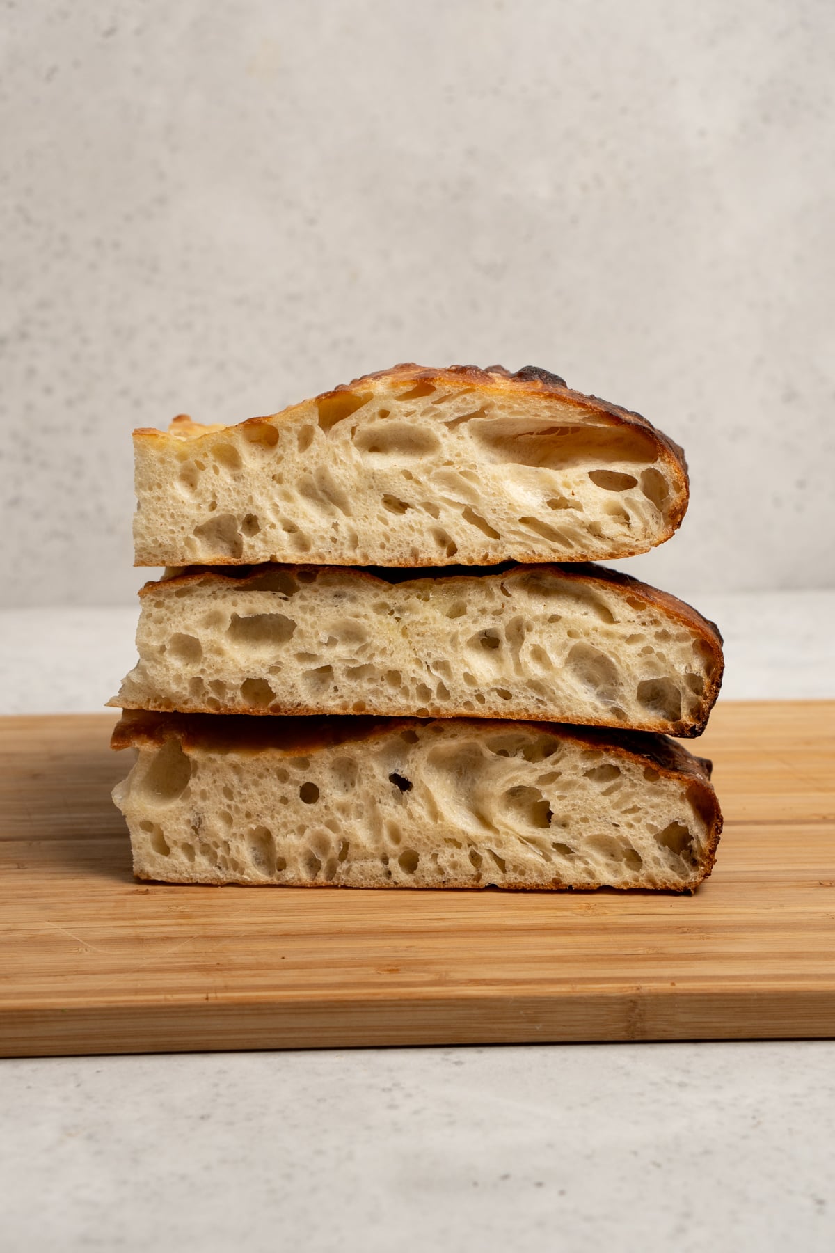 Three pieces of focaccia stacked on top of each other on a wooden cutting board