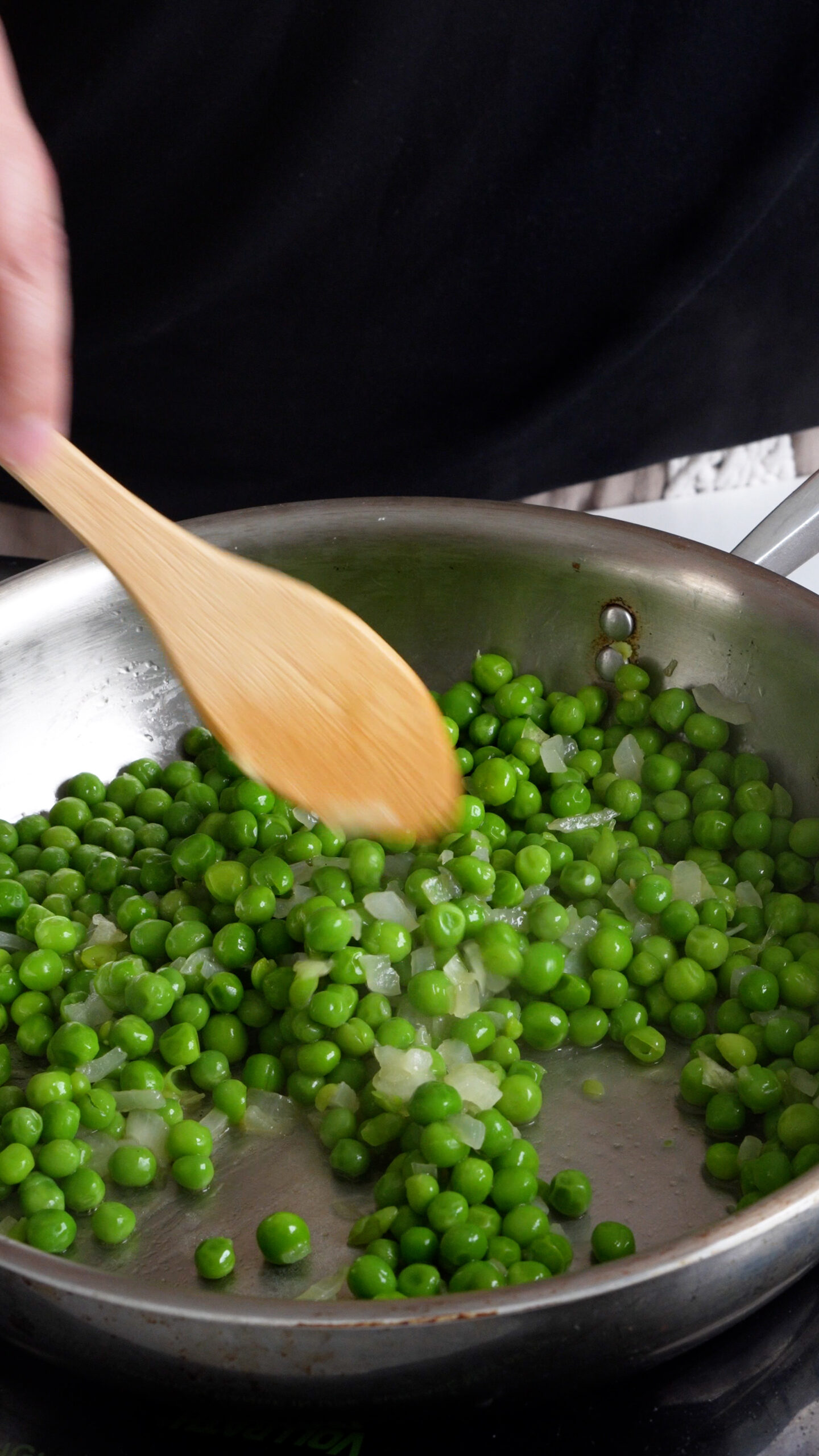 Peas being cooked with onions in a pan