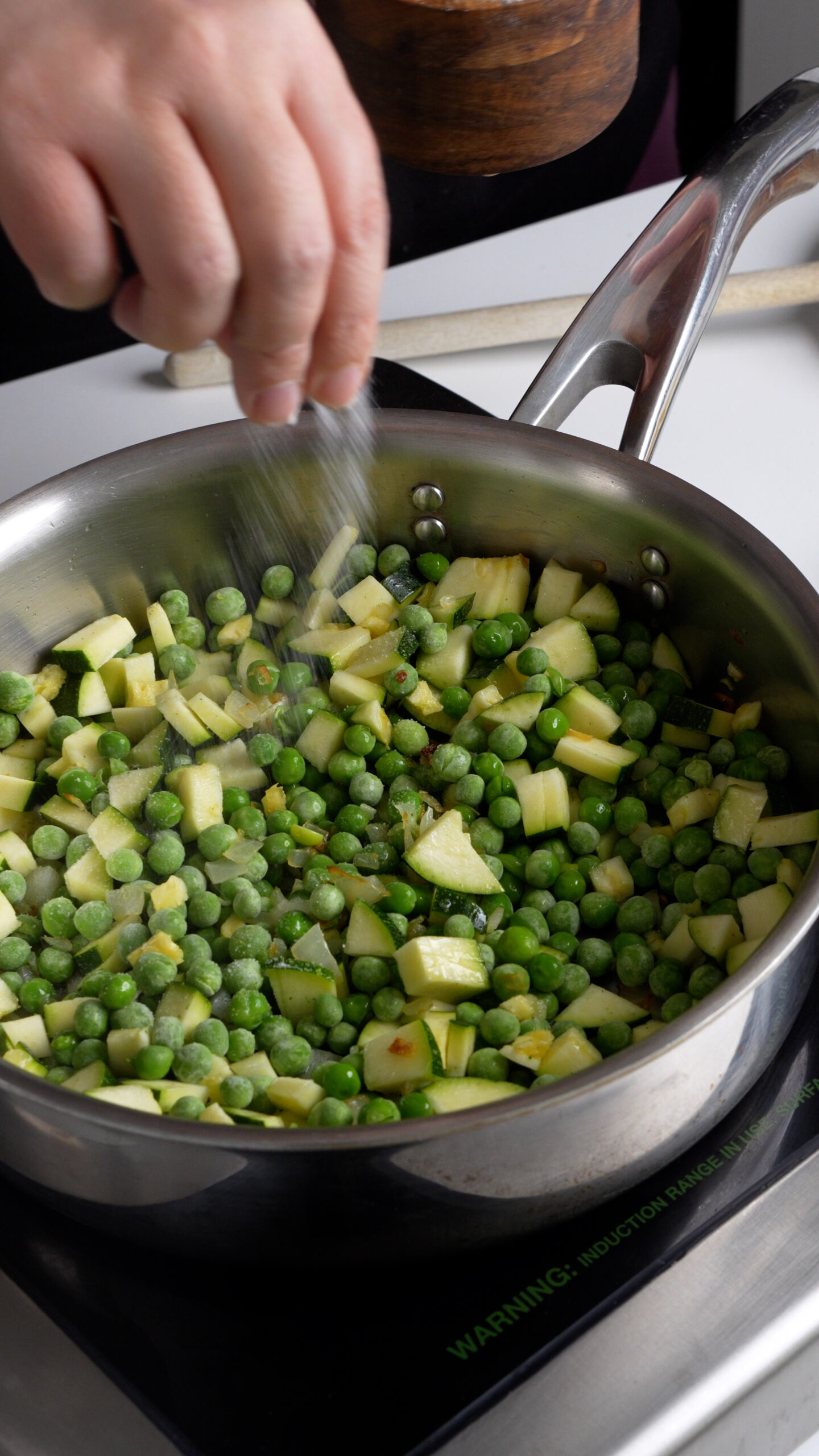 Frozen peas and diced zucchini in a pan being seasoned with salt