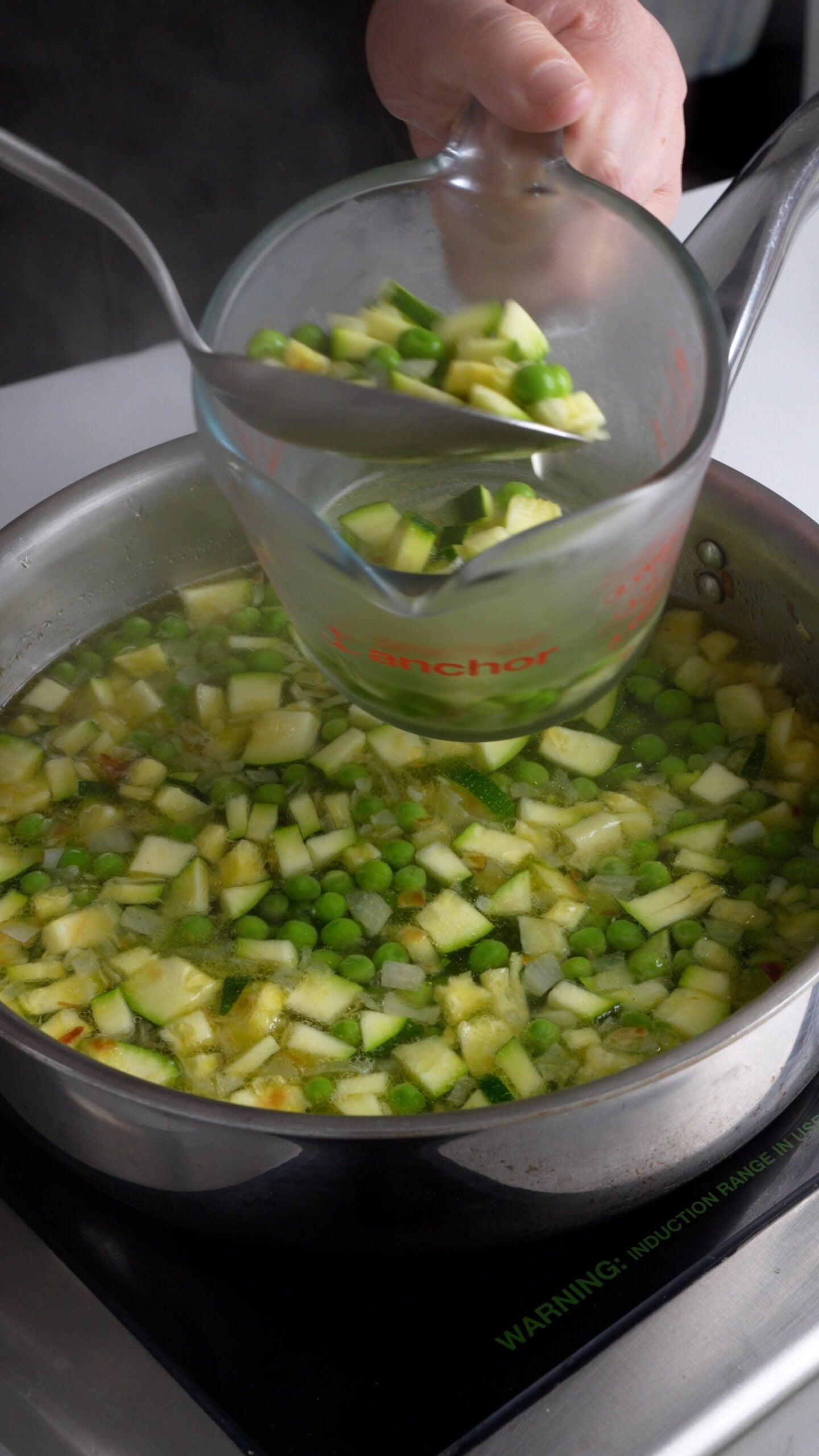 Peas and diced zucchini being placed into a measuring cup