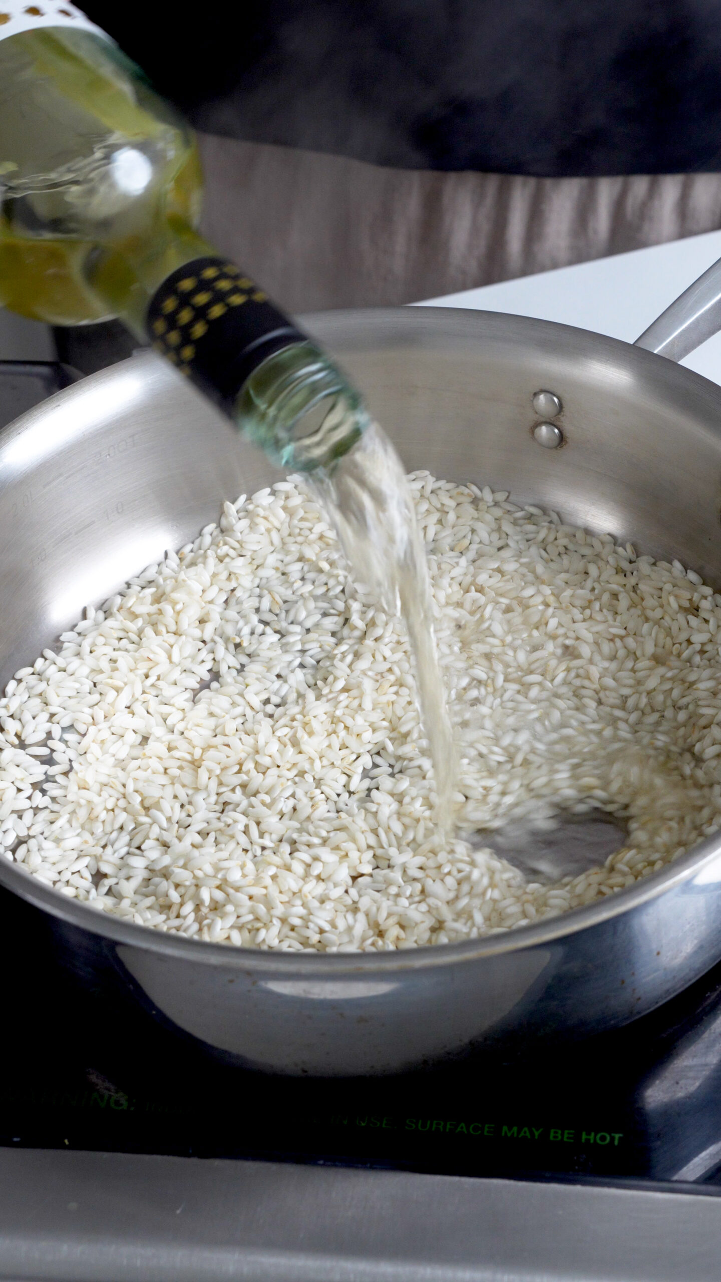 Rice in a pan with white wine being poured in
