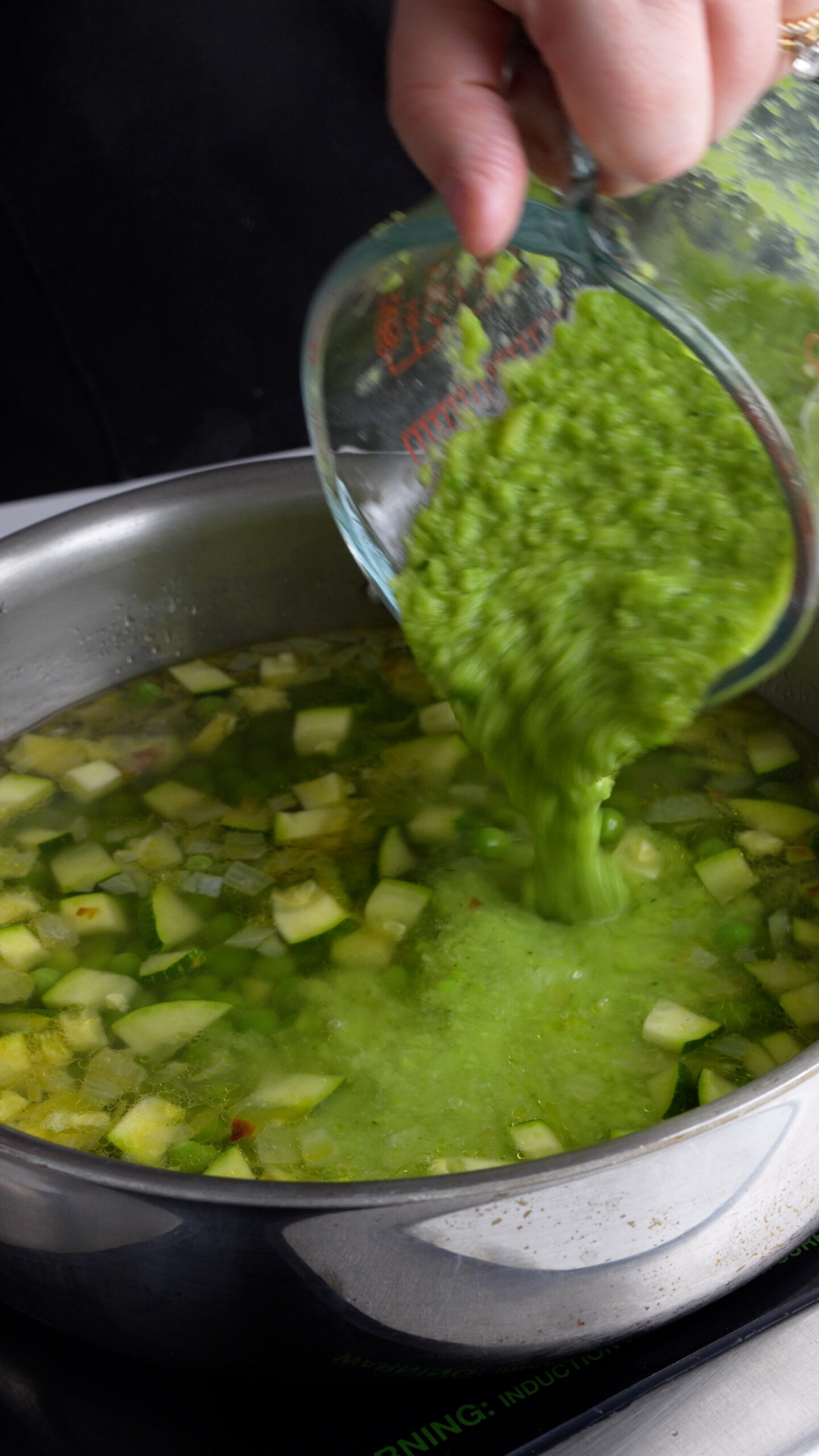 Pea and zucchini purée being poured into a pan with diced zucchini and peas in it