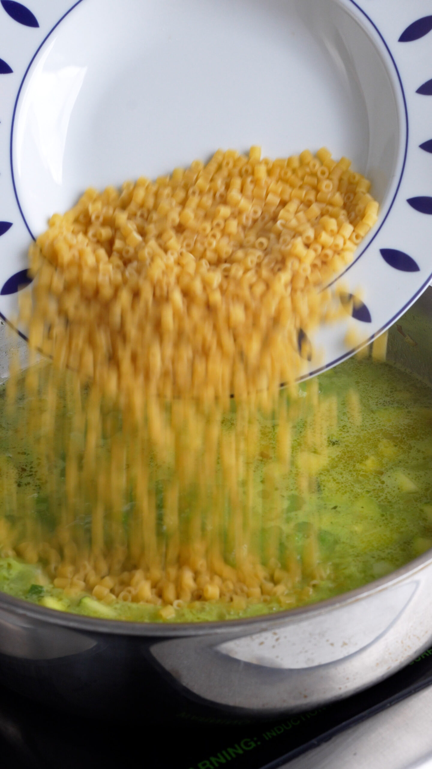 Ditali pasta being added to a pan with zucchini and peas in it
