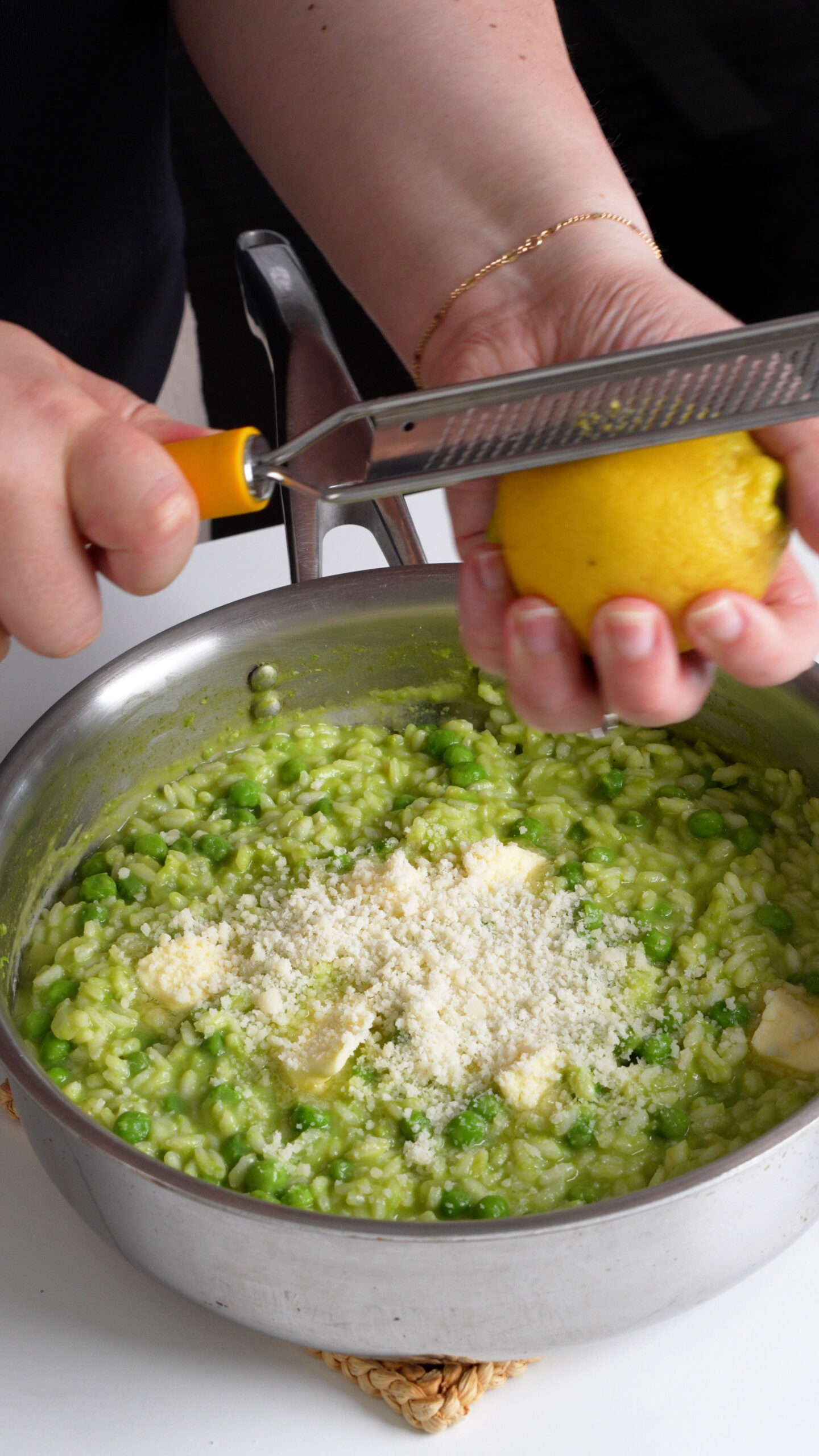 A pan of pea risotto with butter and parmigiano and lemon zest being grated in