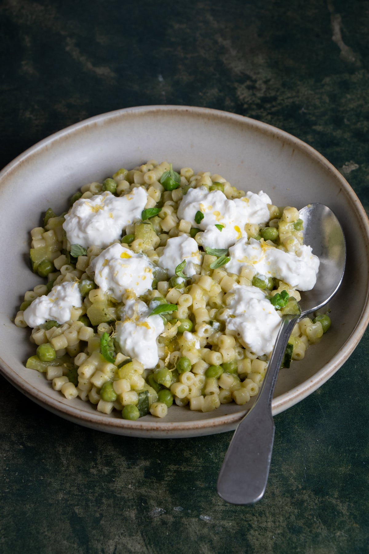 Pasta with peas and zucchini in a plate topped with dollops of burrata