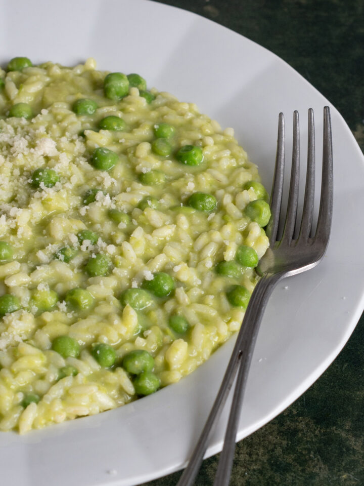 Risotto with peas in a plate topped with gratd parmigiano reggiano