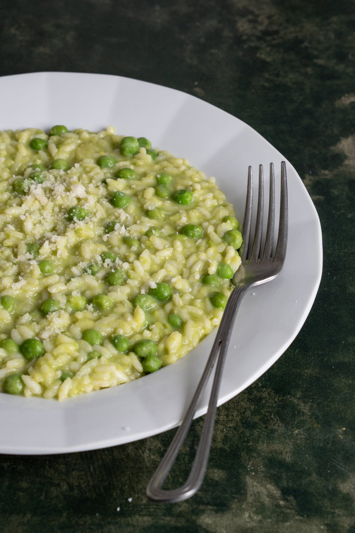 Pea risotto iin a plate topped with grated parmigiano reggiano