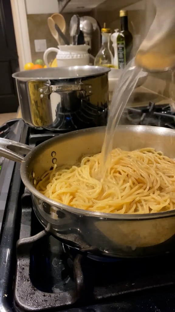 Pasta in a pan with pasta water being added with a ladle