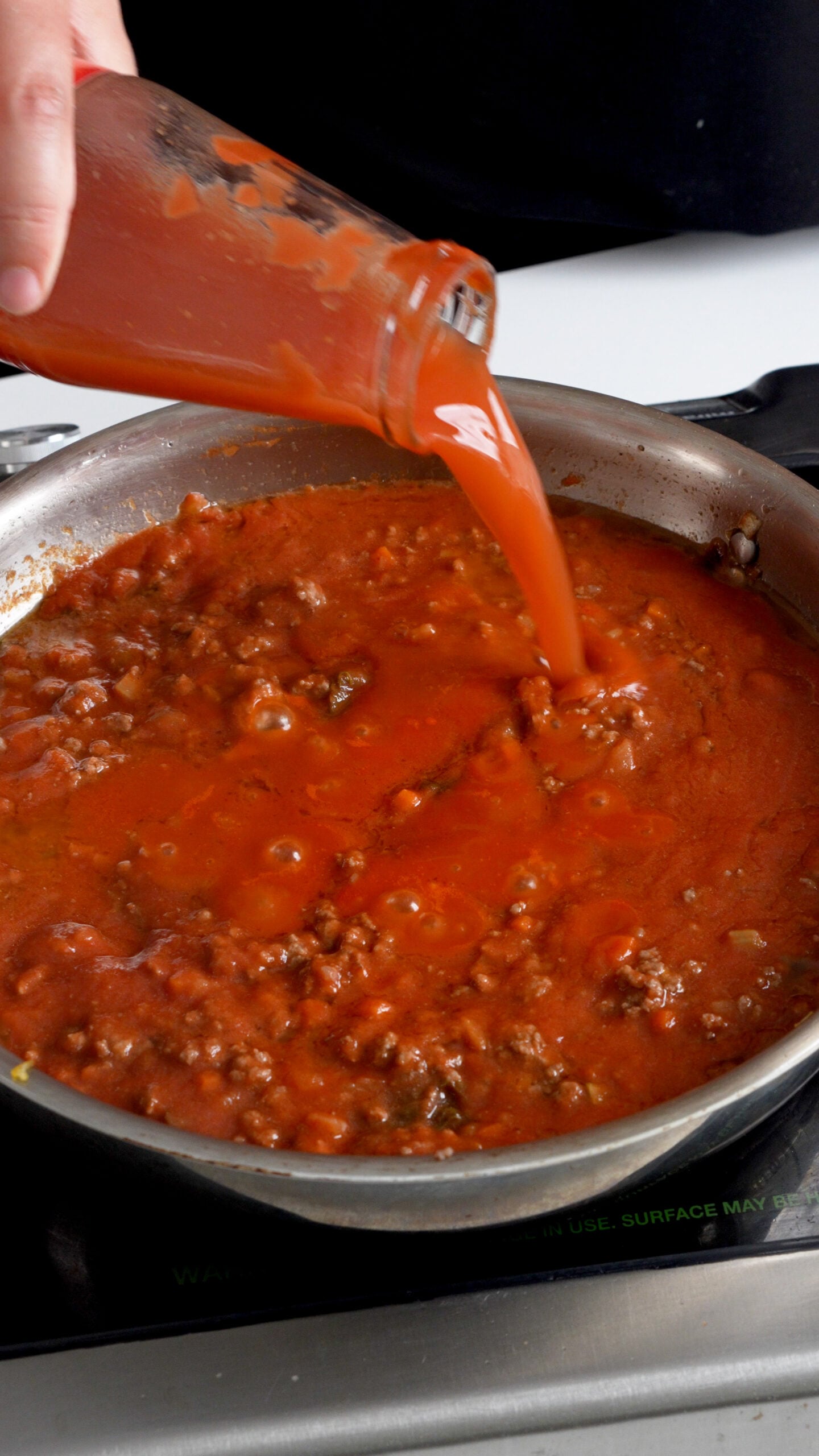 Tomato water being added to a pan with tomato passata in it and ground beef