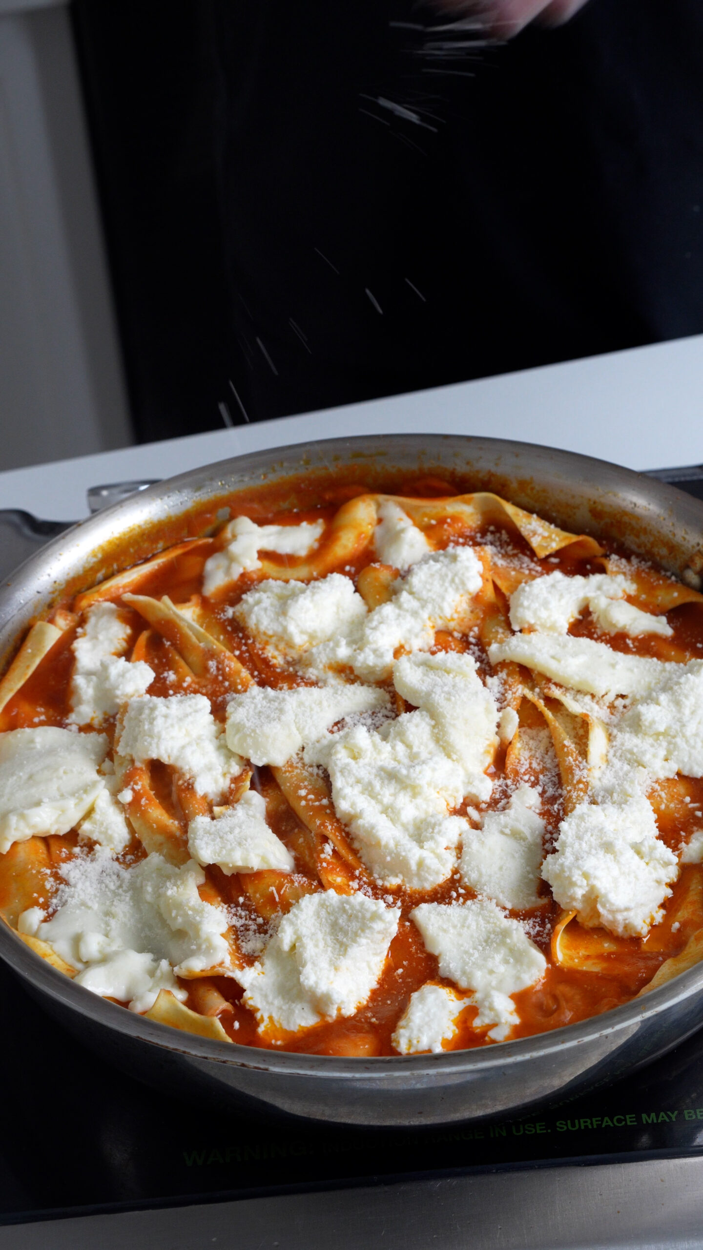 Lasagna in a pan topped with ricotta, mozzarella and parmigiano reggiano