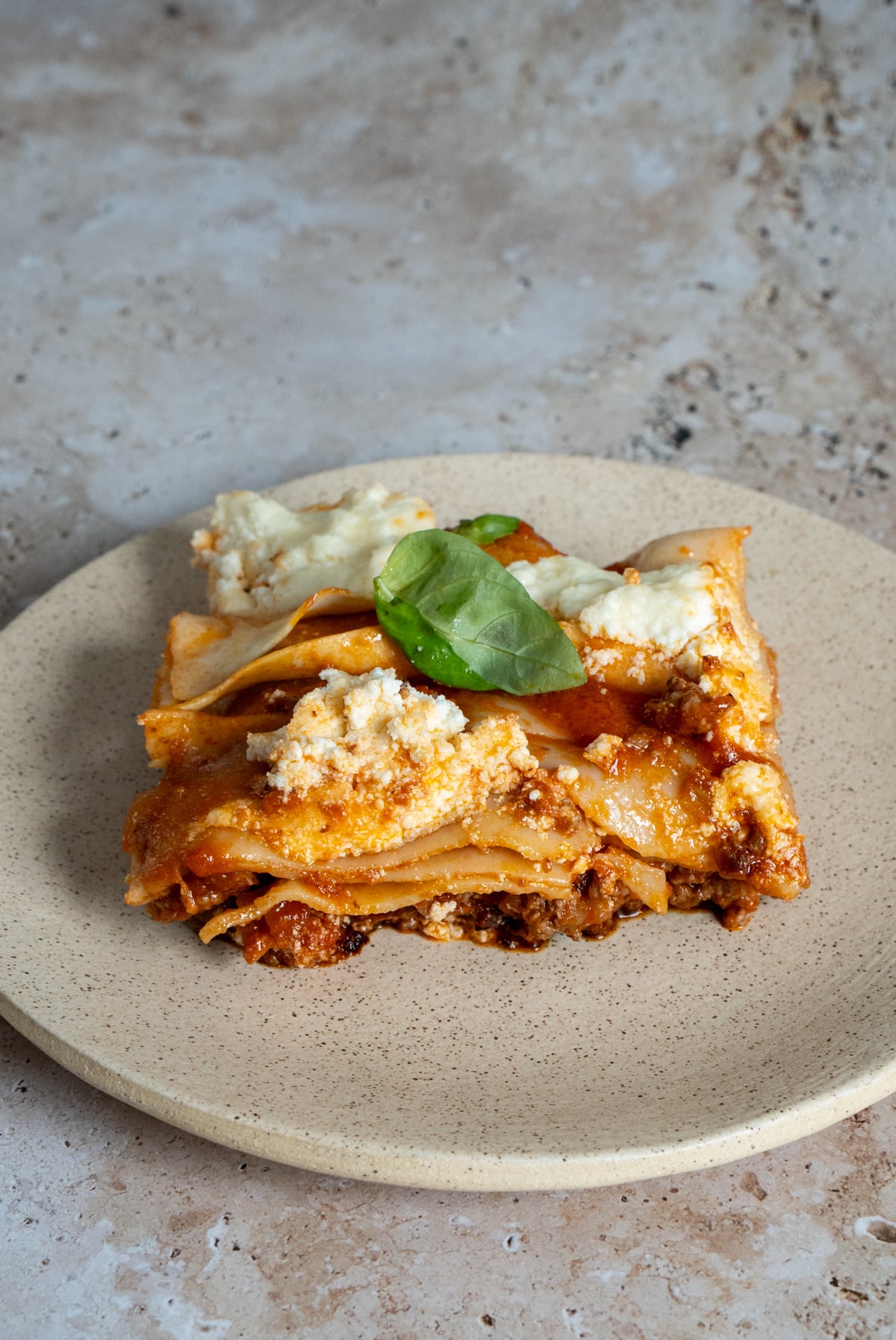 Piece of lasagna in a plate topped with ricotta and fresh basil