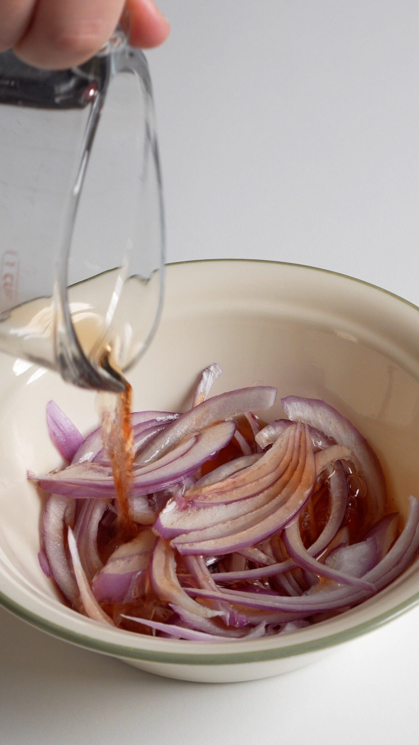 Red wine vinegar being poured onto sliced onions in a bowl