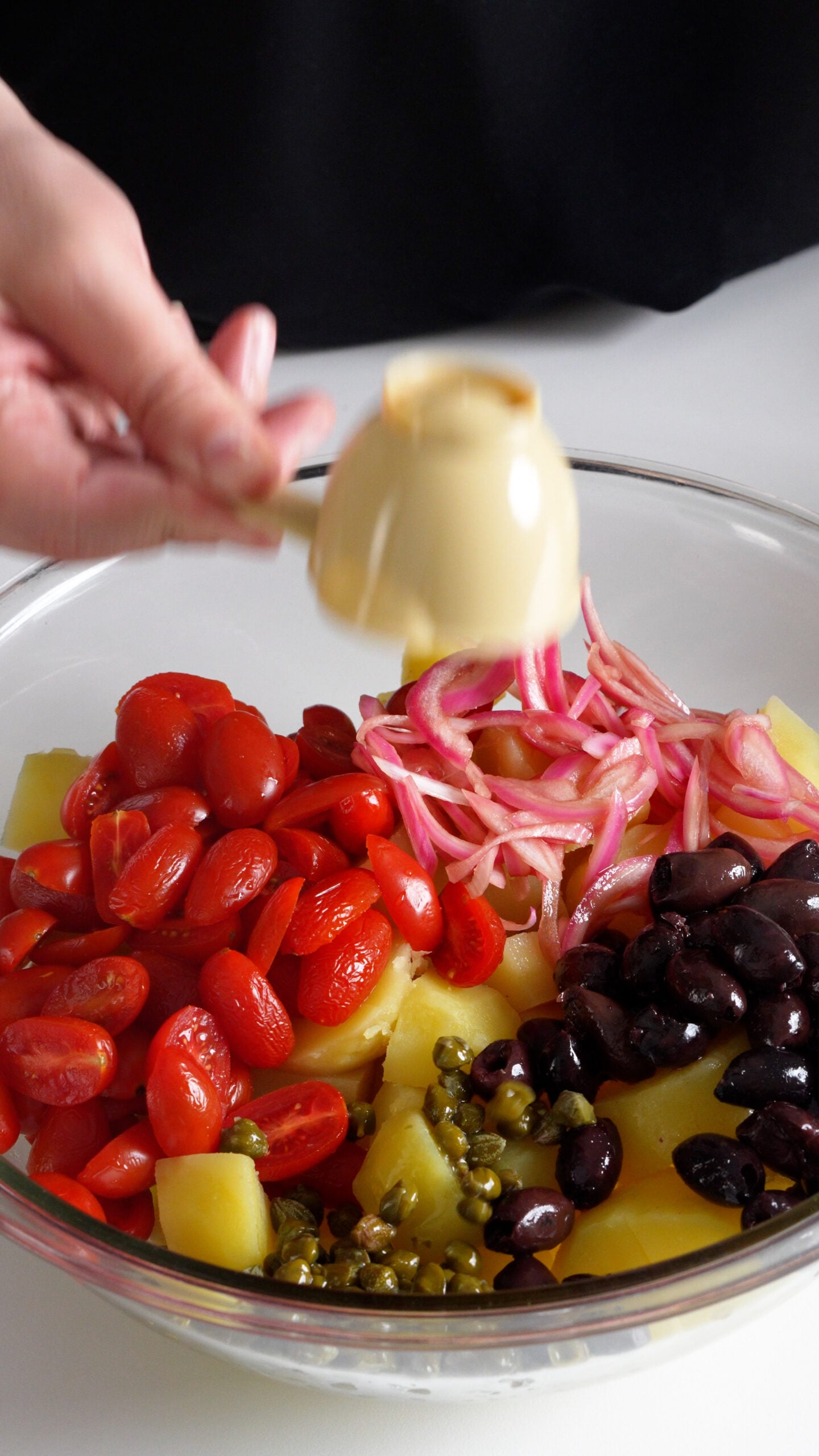 Bowl of boiled potatoes topped with tomatoes, pickled onions, olives and capers
