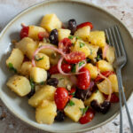 Italian potato salad in a bowl with onions, tomatoes, olives, capers, basil and oregano