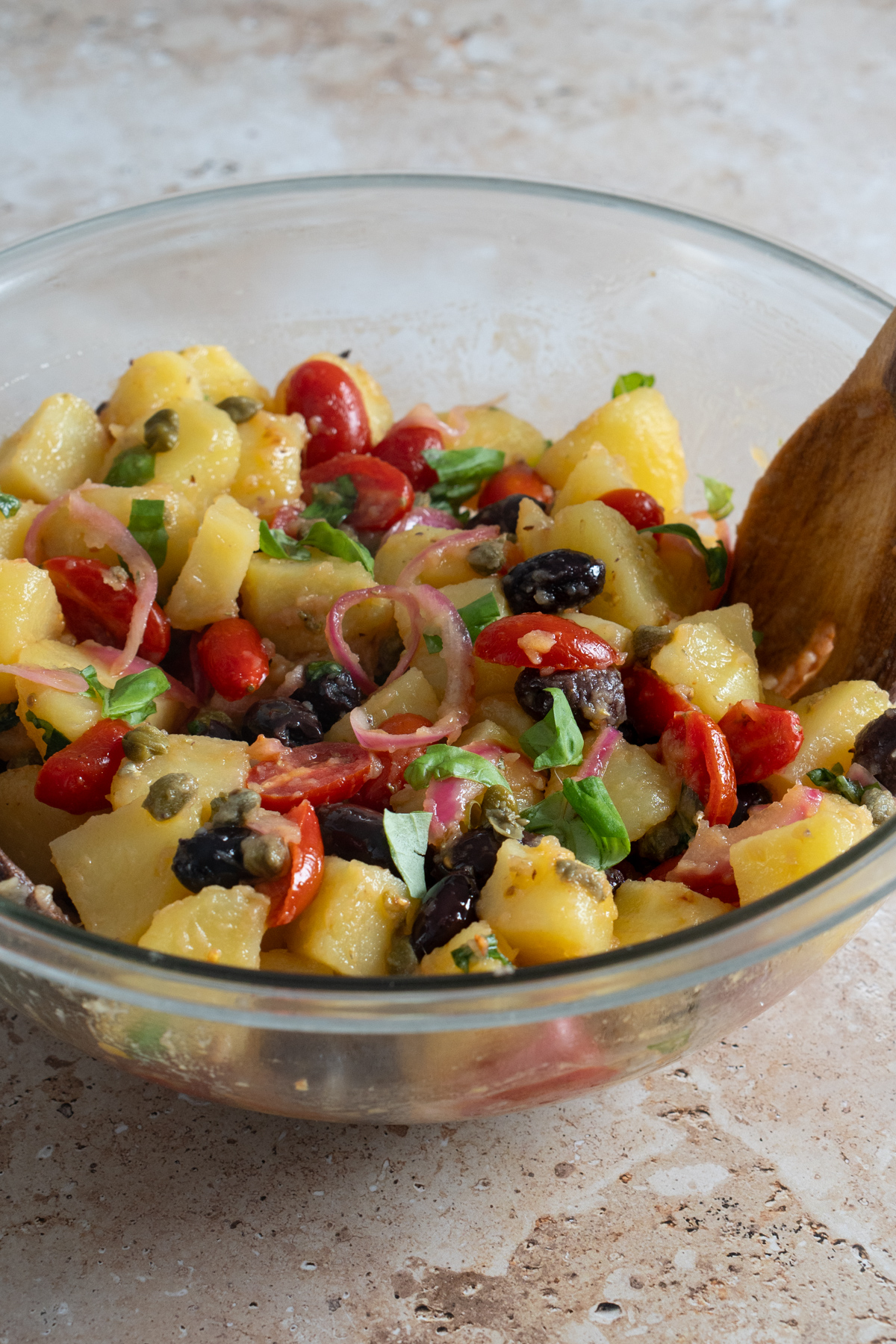 Italian potato salad in a bowl with fresh tomatoes, olives, pickled onions, capers and basil