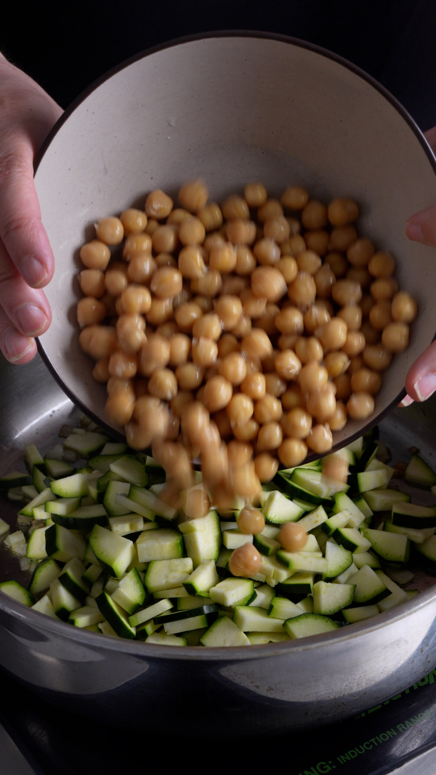 Chick peas being poured into a pan with sliced zucchini