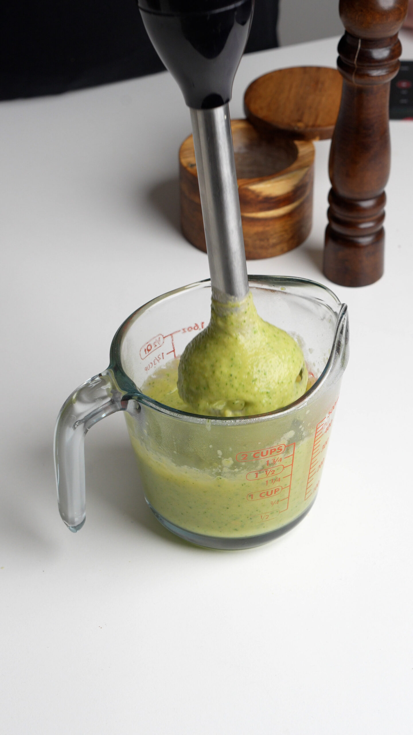 Zucchini and chick peas being blended in a measuring cup with an immersion blender