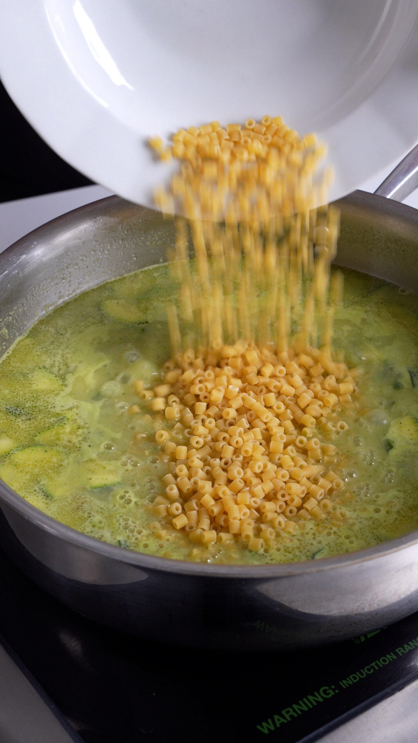 Pasta being poured into a pan with zucchini and chick peas