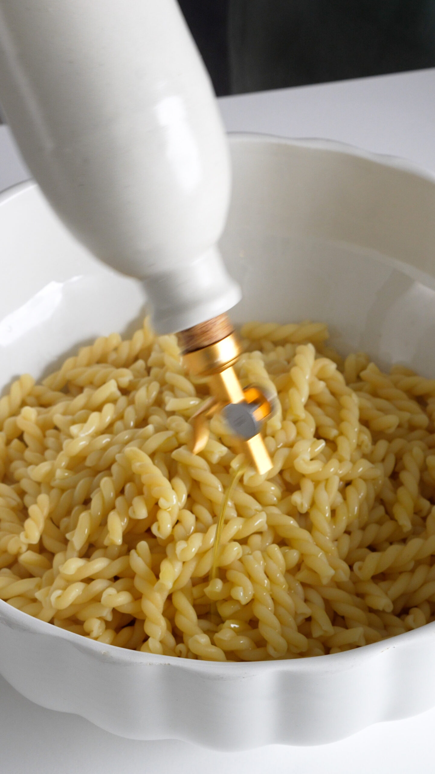 Olive oil being drizzled onto cooked pasta in a bowl
