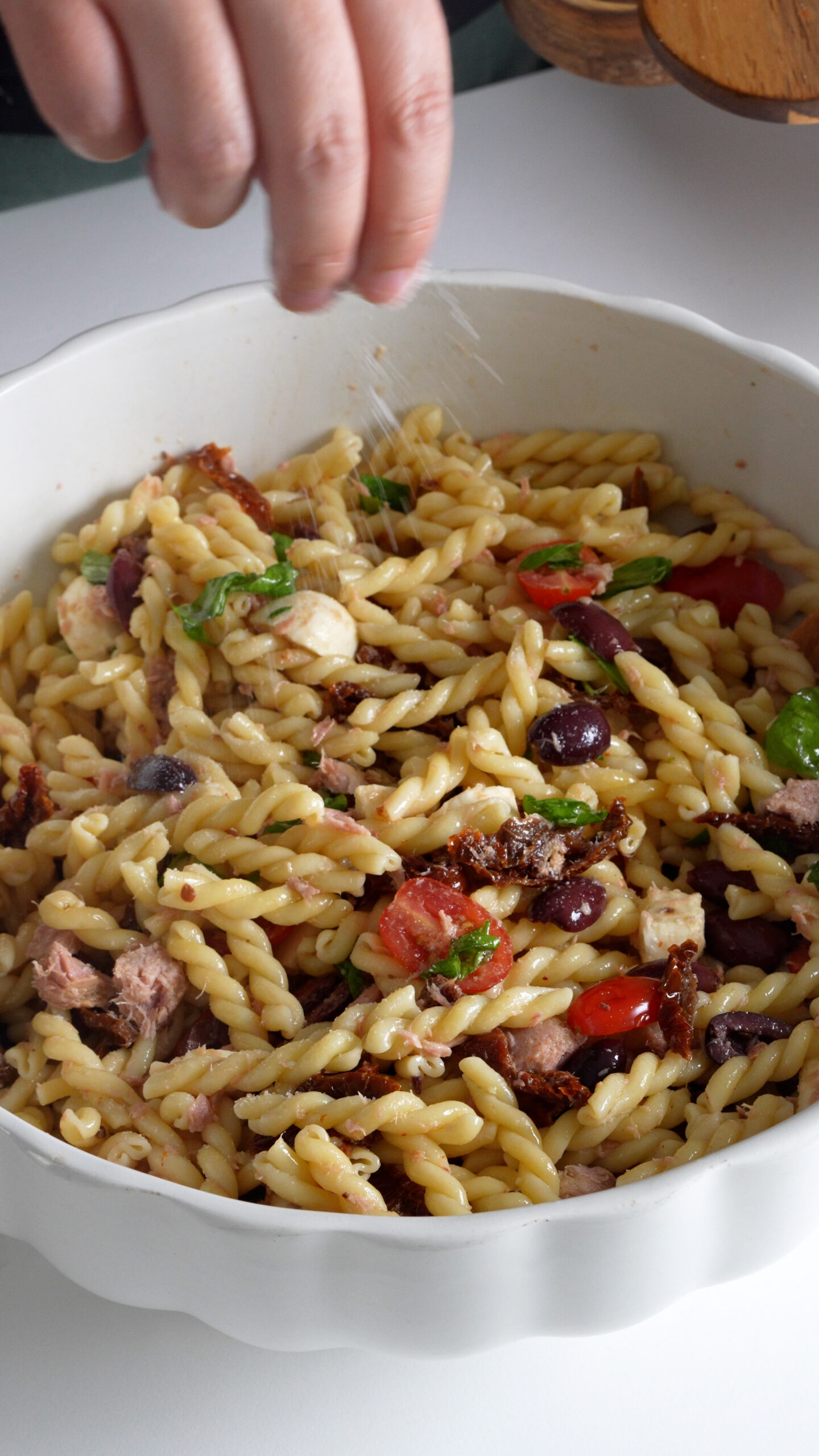 Pasta salad being seasoned with salt
