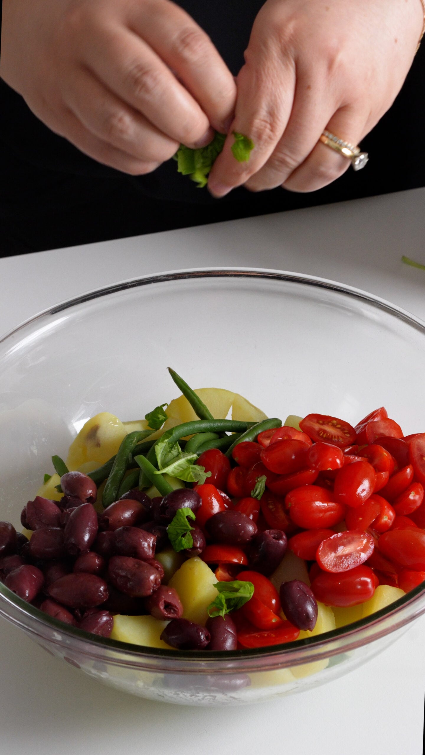Potatoes, green beans, tomatoes, olives, fresh basil in a large glass bowl