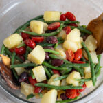 Potato salad with green beans with tomatoes and olives in a glass bowl.