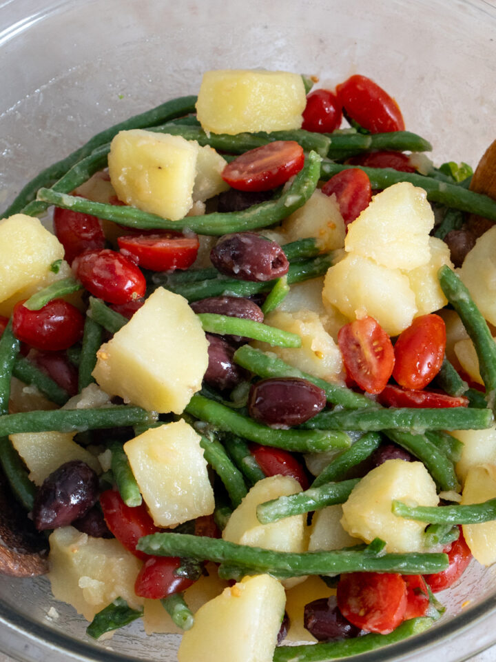 Potato salad with green beans with tomatoes and olives in a glass bowl.