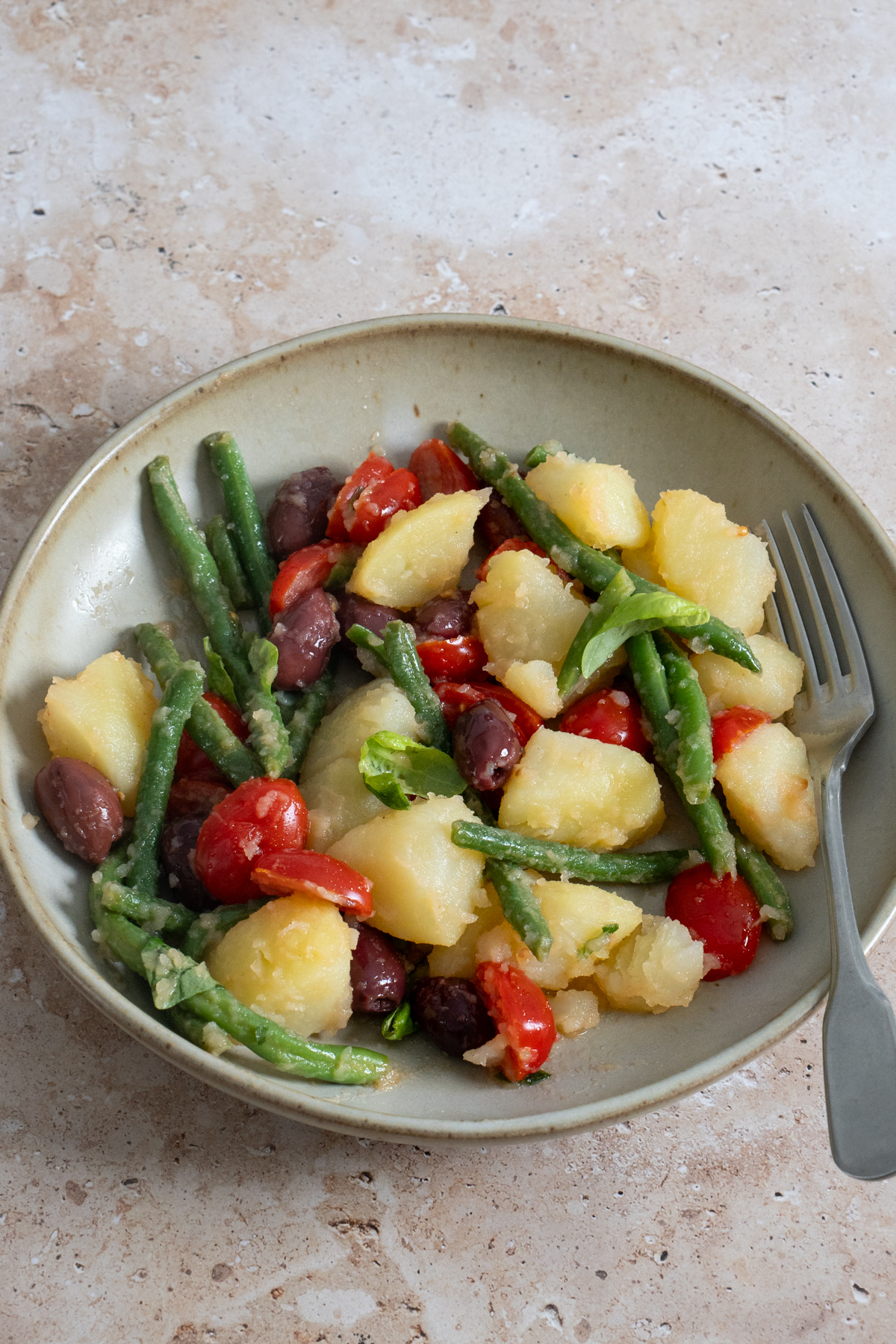 Potato salad with green beans, tomatoes and olives in a plate with a fork to the side