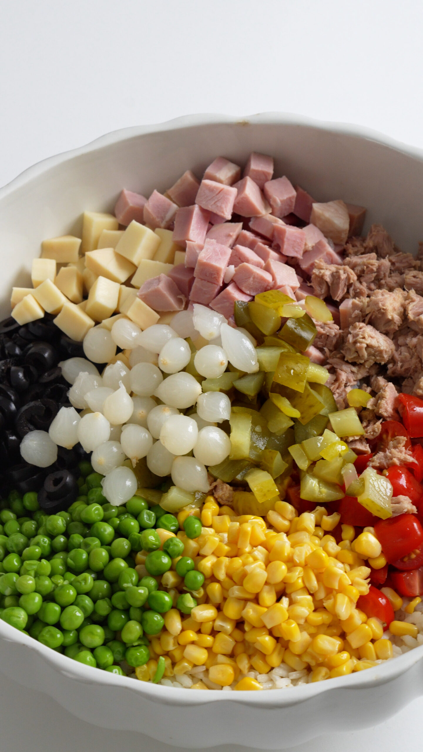 Bowl of rice with ham, tuna, tomatoes, corn, peas, olives, cheese, pickles and onions on top