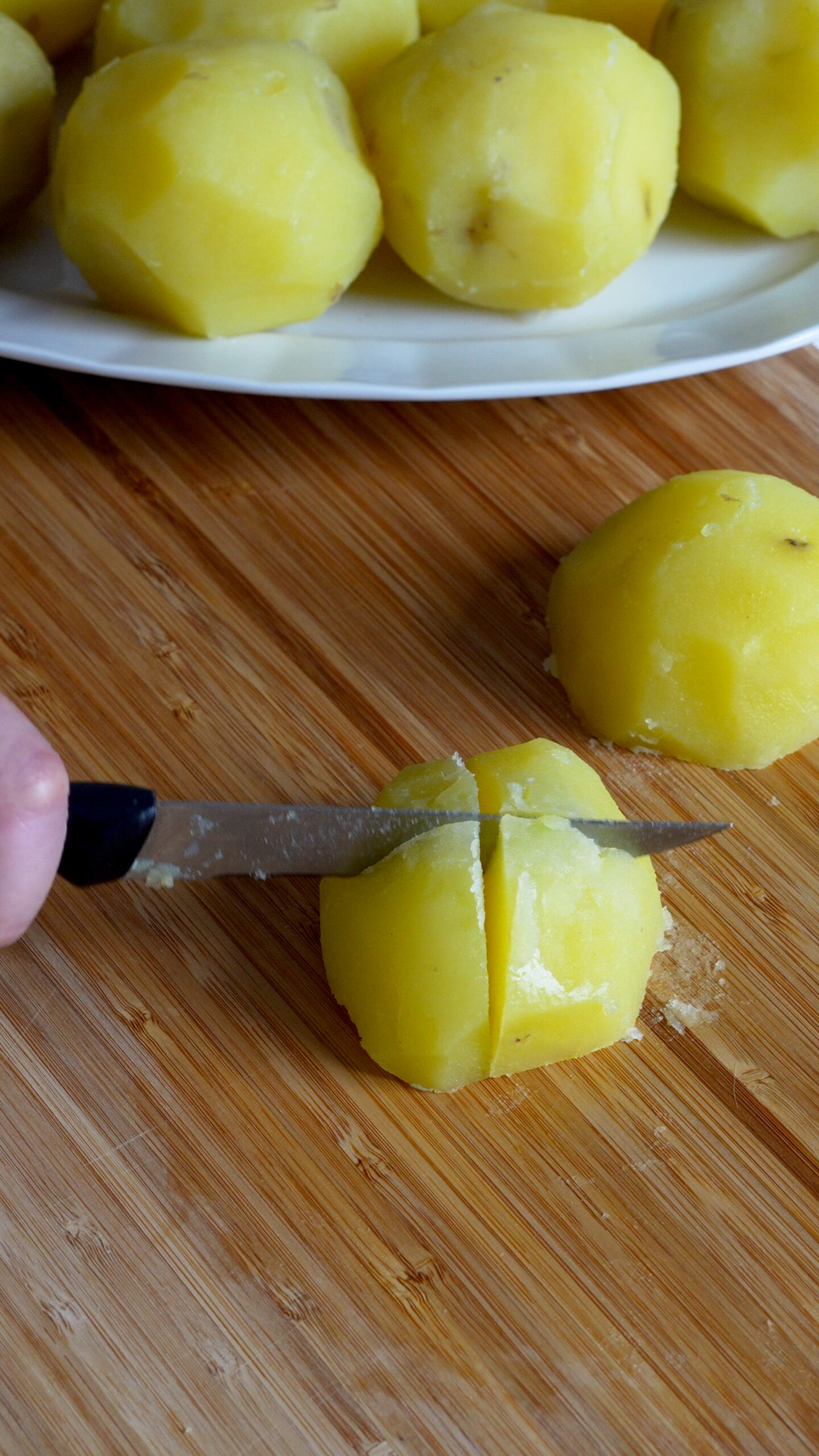 Boiled peeled yukon gold potatoes being cut with a knife